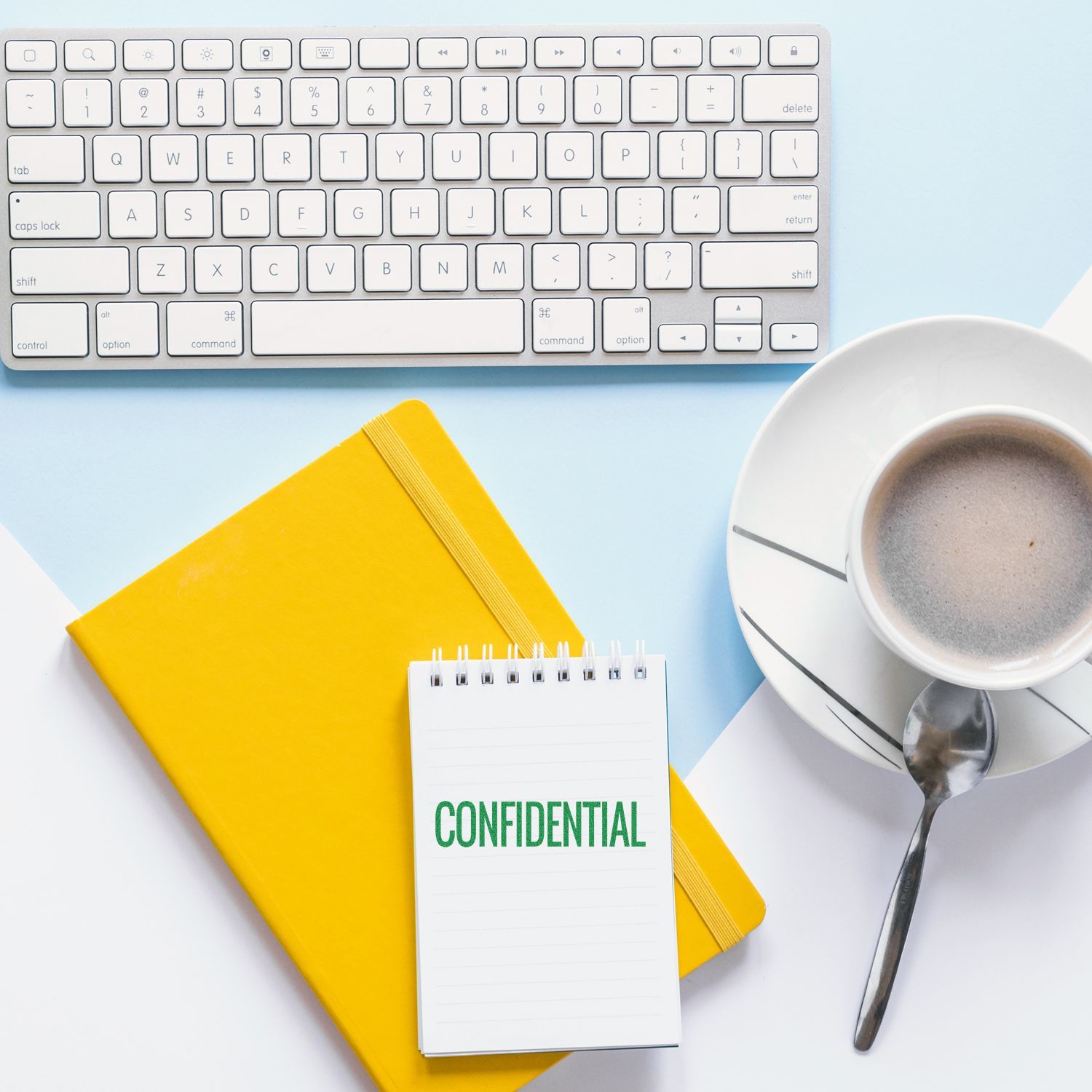Flat lay of office desk with computer keyboard, yellow notebook, confidential notepad, and coffee cup on a clean blue background.