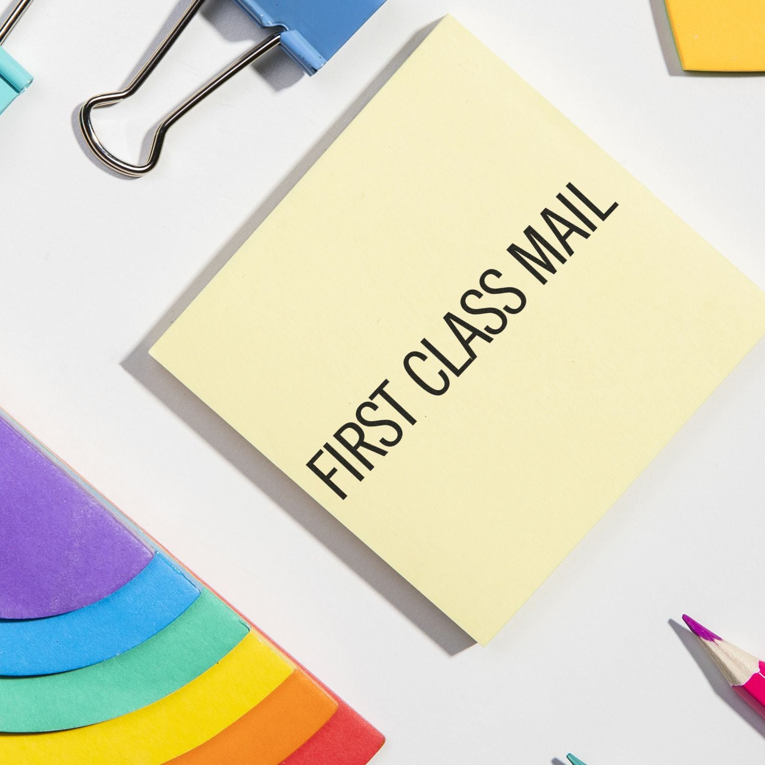 First class mail sticky note with colorful office supplies on a white desk background