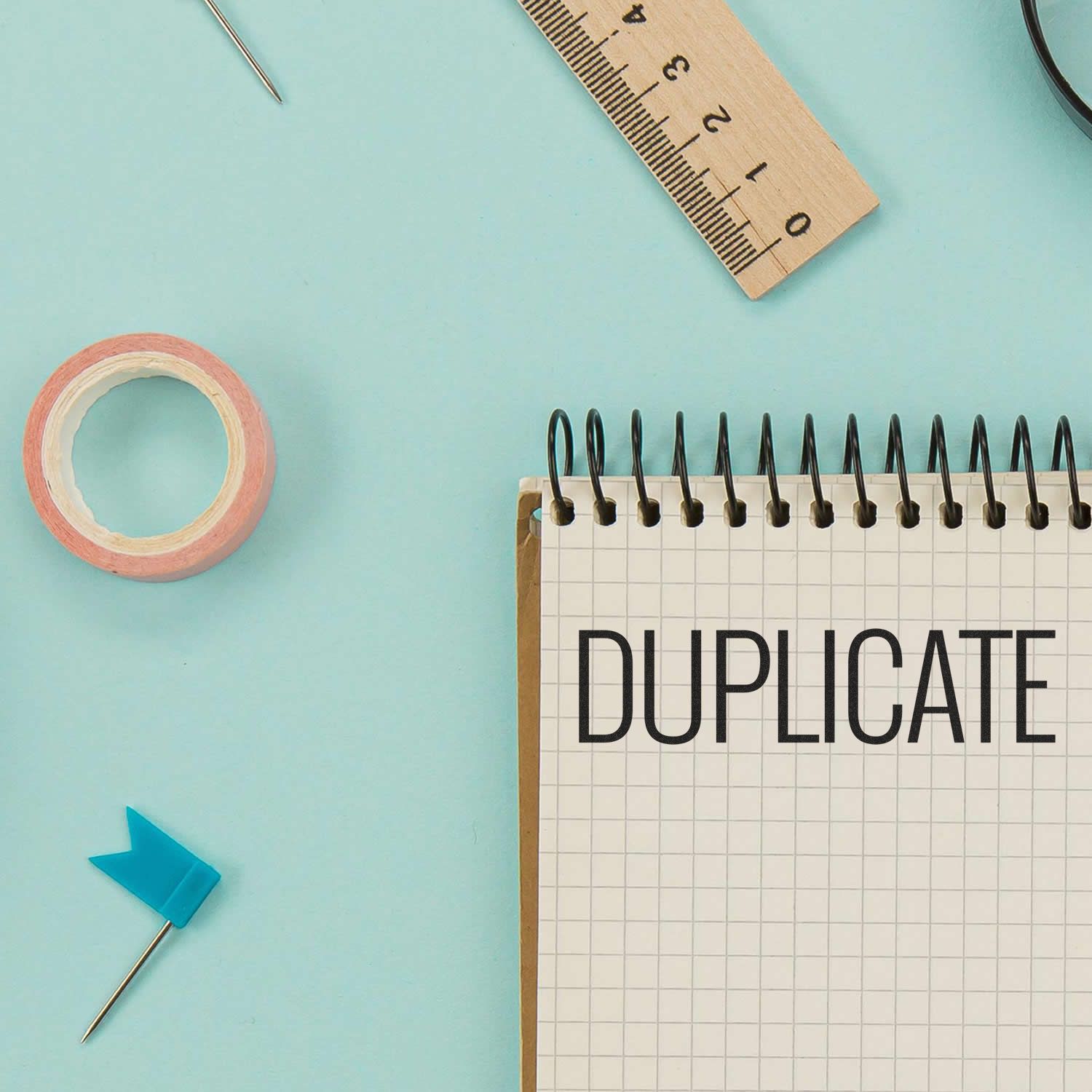 Duplicate paperwork concept with notebook reading DUPLICATE and measurement tools like ruler, tape, and pushpins on a blue desk background