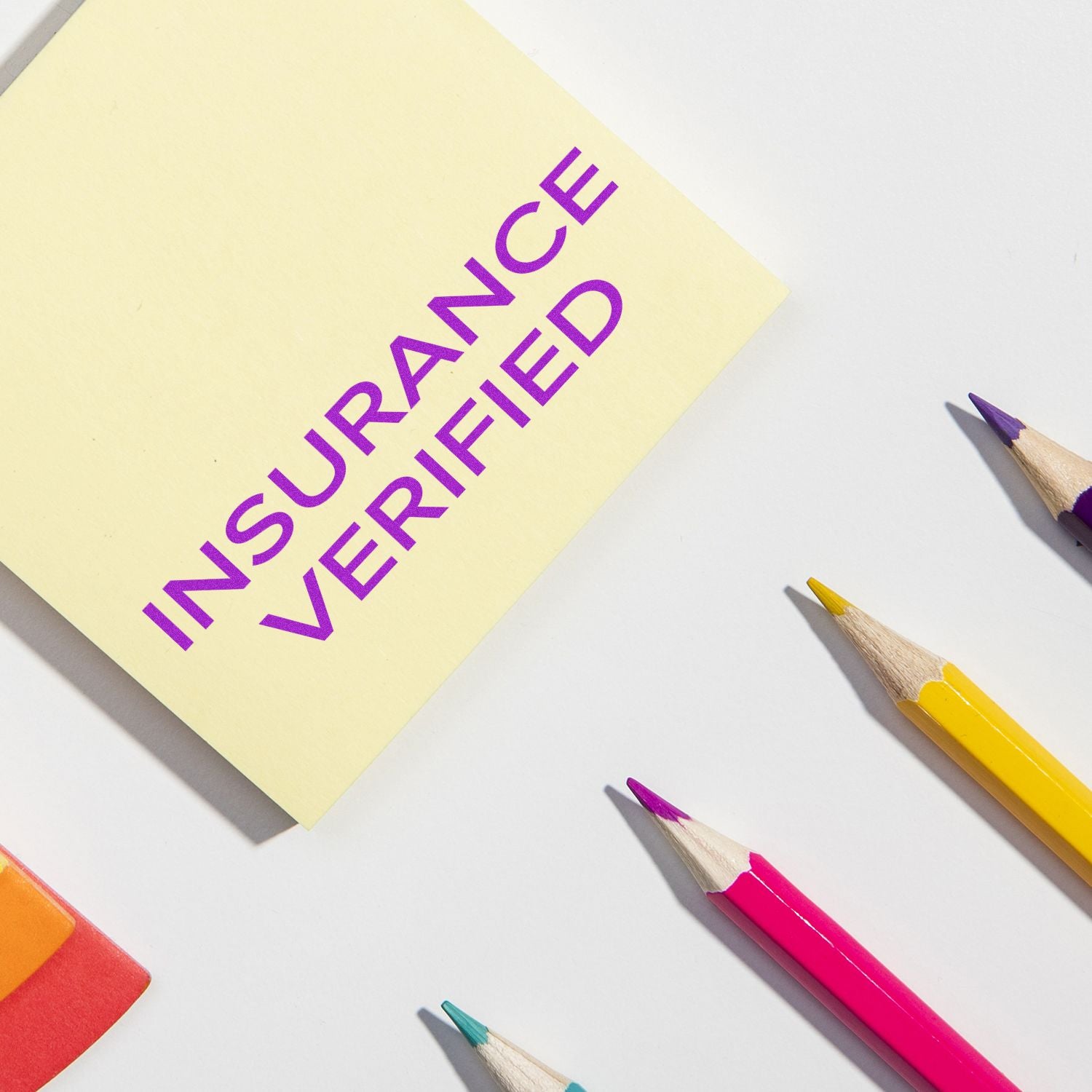 Insurance verified message on yellow sticky note with colored pencils, symbolizing verified coverage and policy confirmation.