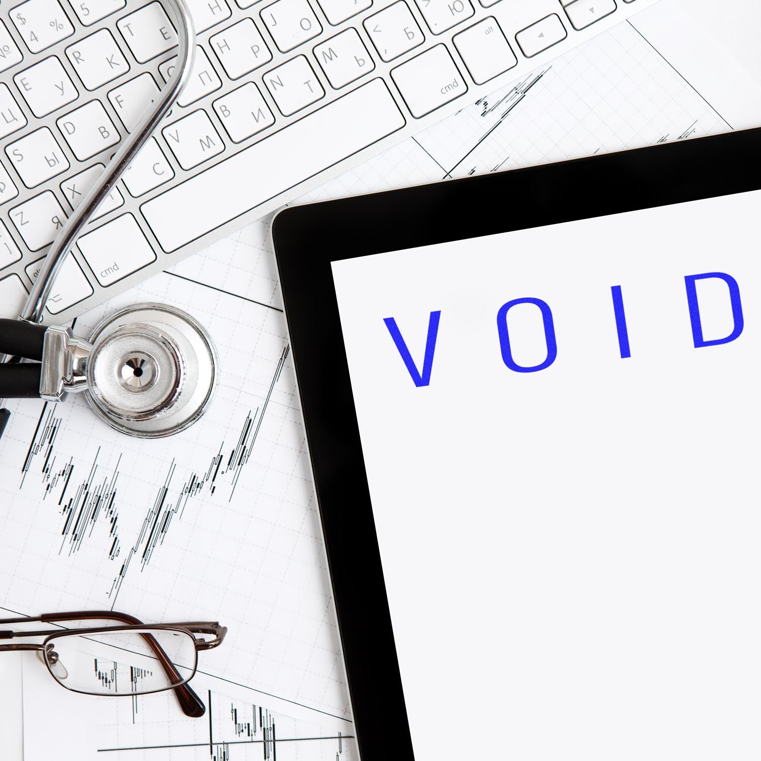 Stethoscope on keyboard beside tablet displaying VOID, eyeglasses, and stock market chart.