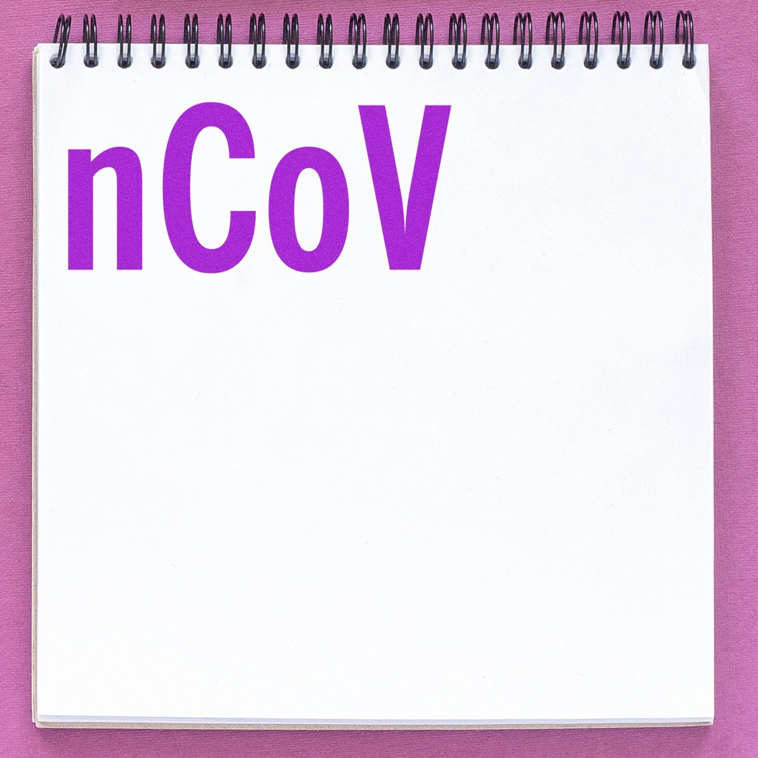 Purple nCoV text on a spiral notebook page, coronavirus concept on a pink background.