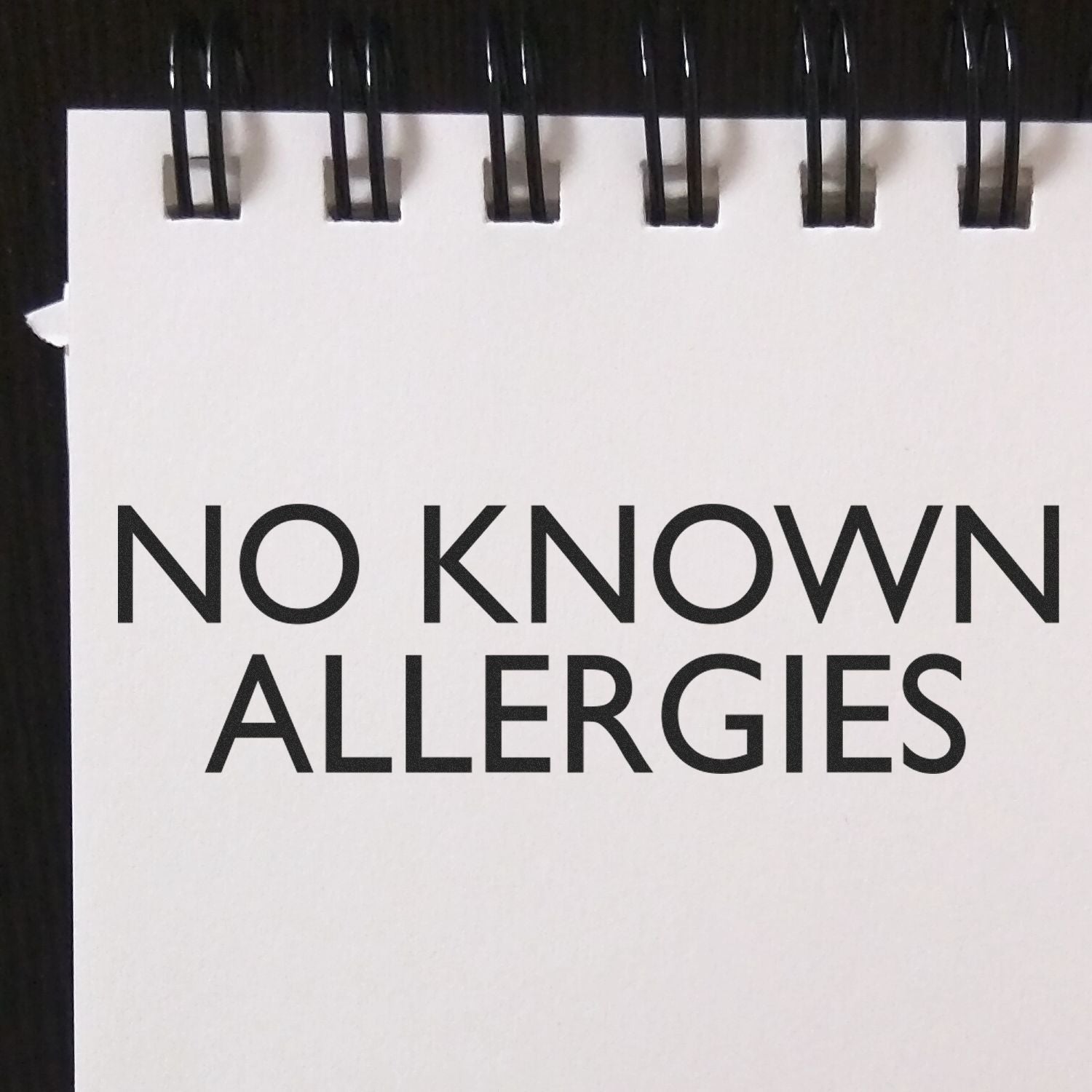 Notebook page with bold text No Known Allergies, a medical allergy alert note on a spiral-bound notepad.