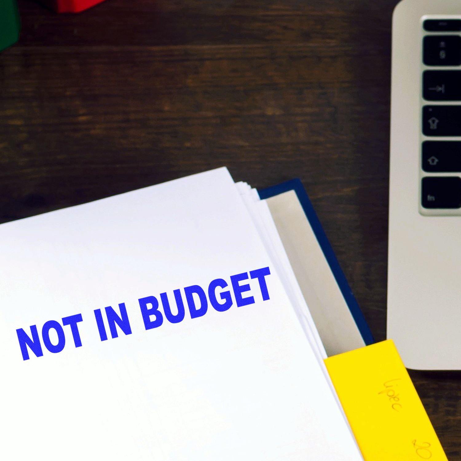 Not in budget document on desk next to laptop and color-coded folders for business budgeting and expense planning