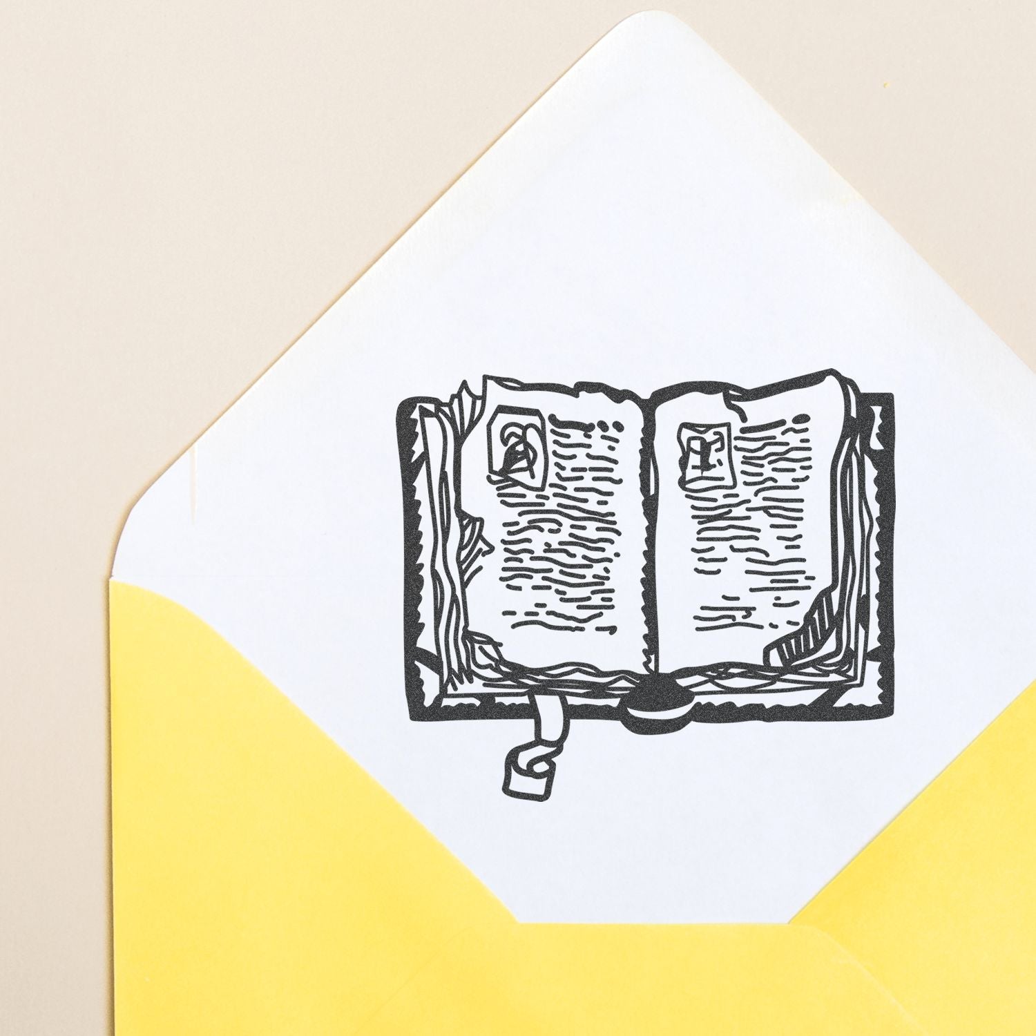 Yellow envelope with a white card featuring a black line art illustration of an open book, ideal for literature, reading, or education themed design.