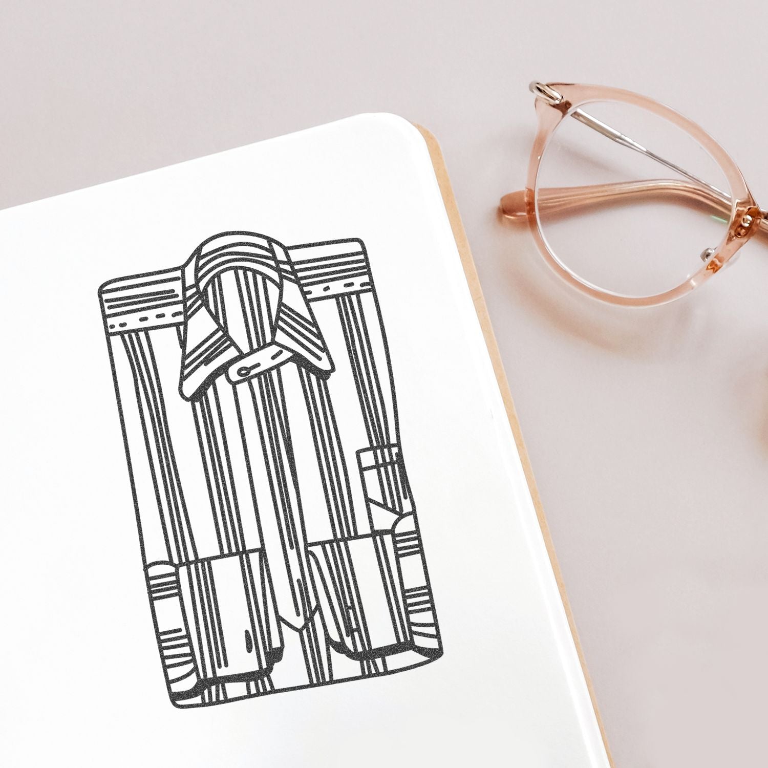 Minimalist notebook with black line art shirt illustration and rose gold eyeglasses on a clean desk background