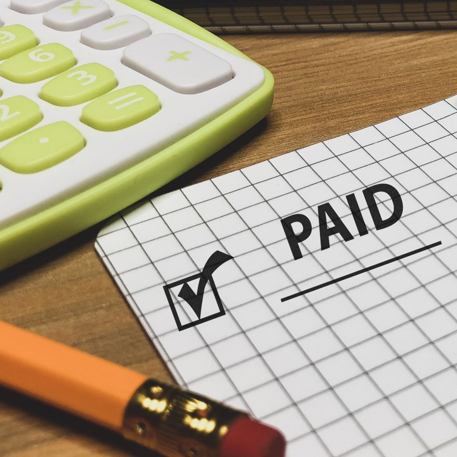 Green calculator on a payment ledger with a PAID stamp, illustrating bookkeeping and settled invoices for accounting.
