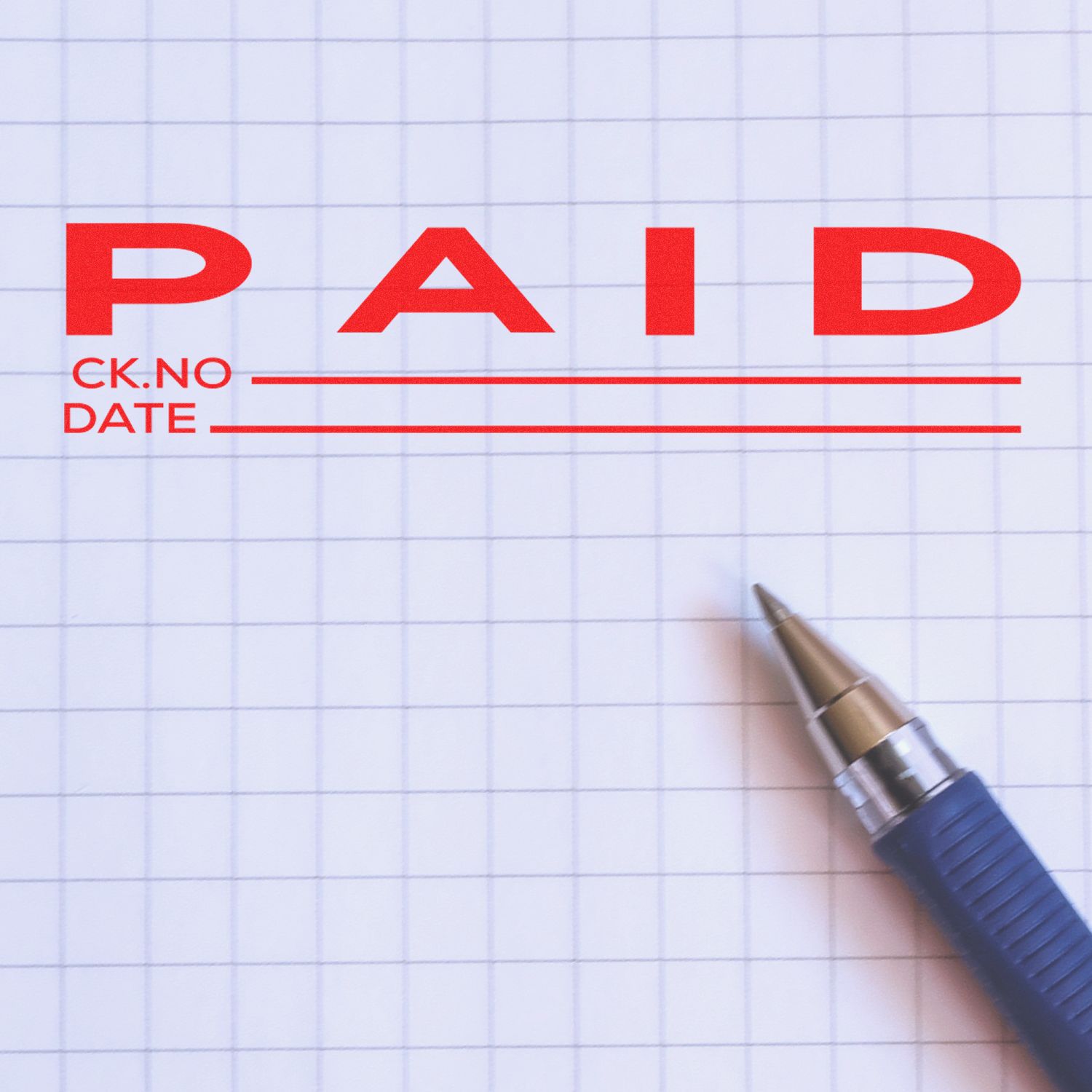 Close-up of a paid check form with red PAID stamp and pen on graph paper background.