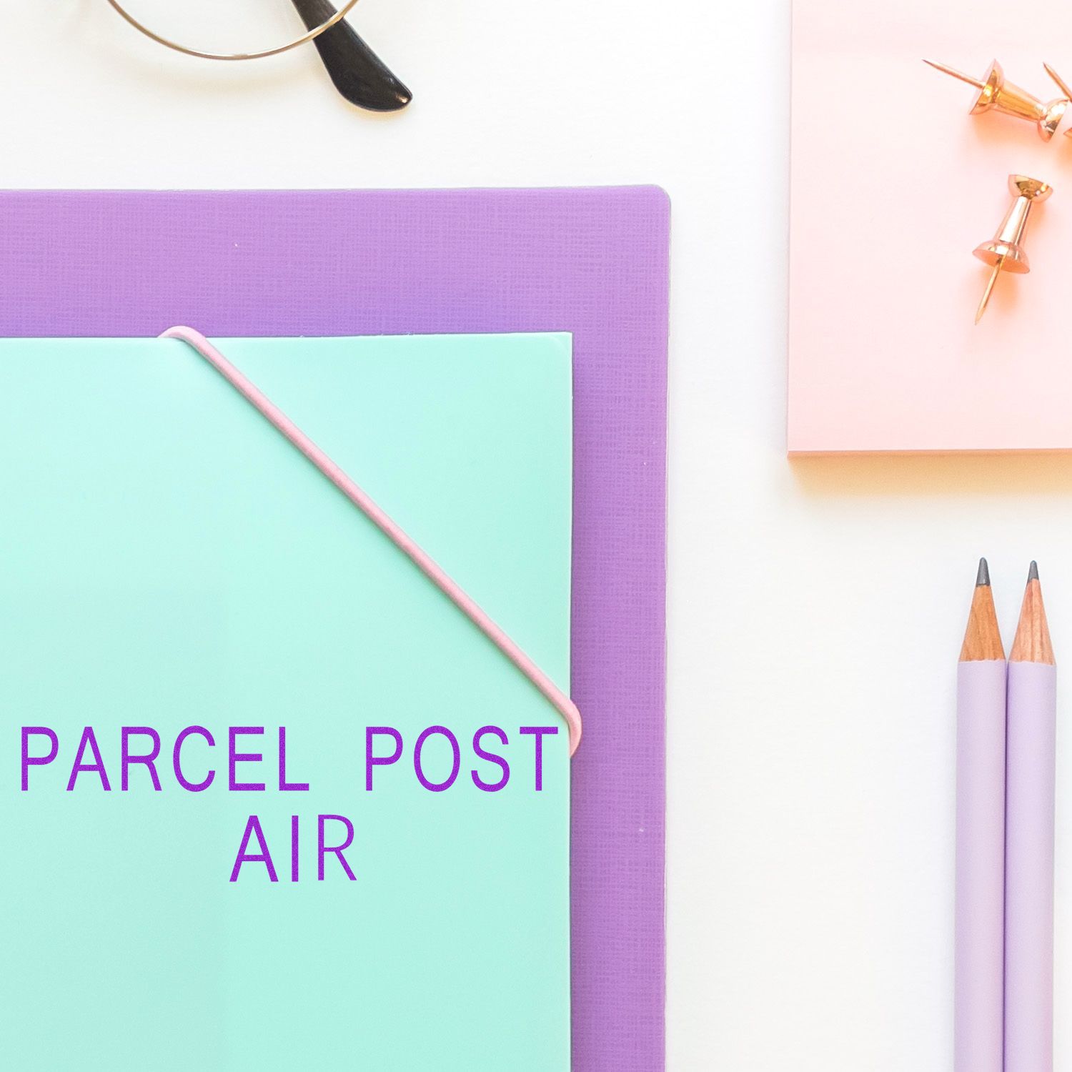 Pastel stationery flat lay with a mint envelope, purple notebook, pencils, push pins, and Parcel Post Air text.
