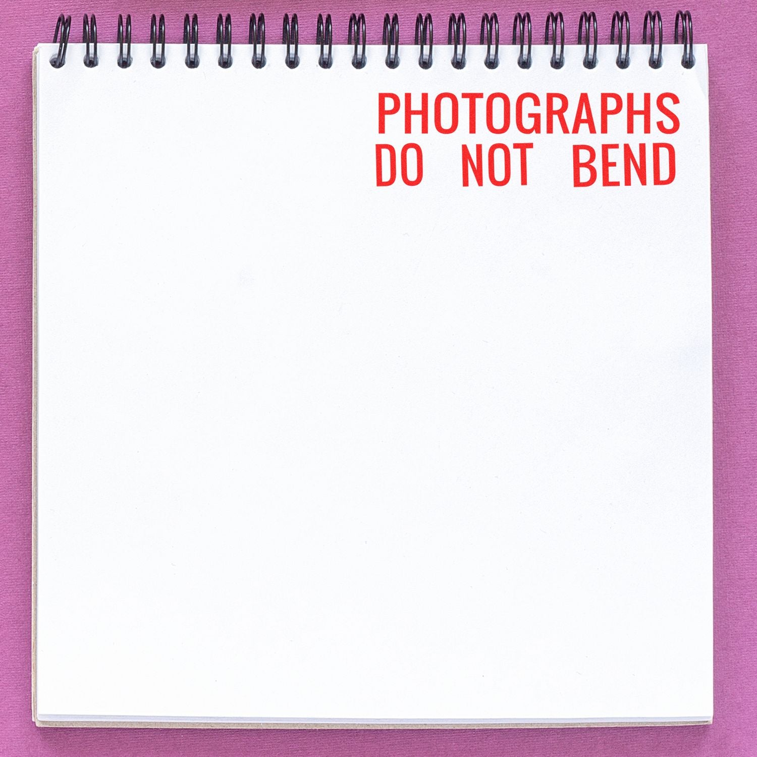Spiral notebook page with red text PHOTOGRAPHS DO NOT BEND on a pink background.