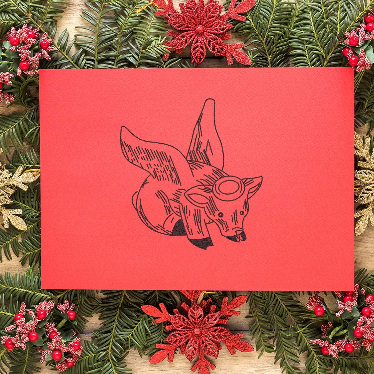 Red holiday greeting card with a fox illustration surrounded by Christmas greenery, red ornaments, and festive winter decorations.
