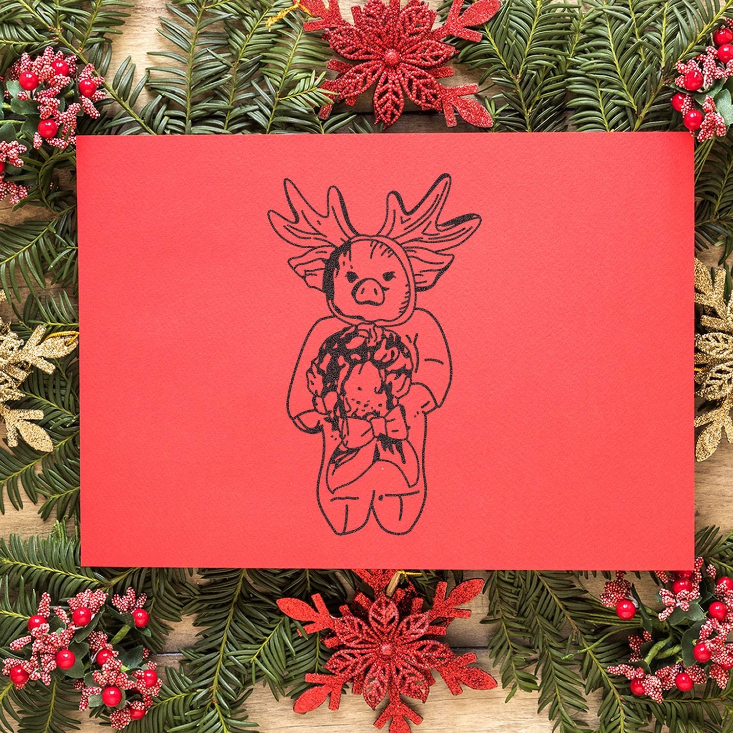 Festive red Christmas card with reindeer pig illustration, surrounded by evergreen branches and holiday decorations.