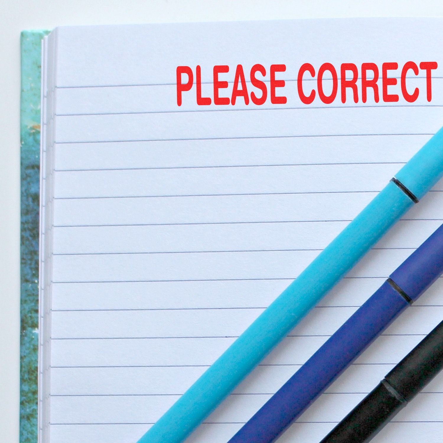 Notebook page with PLEASE CORRECT text and blue pencils, emphasizing document editing, proofreading, and revision guidance.