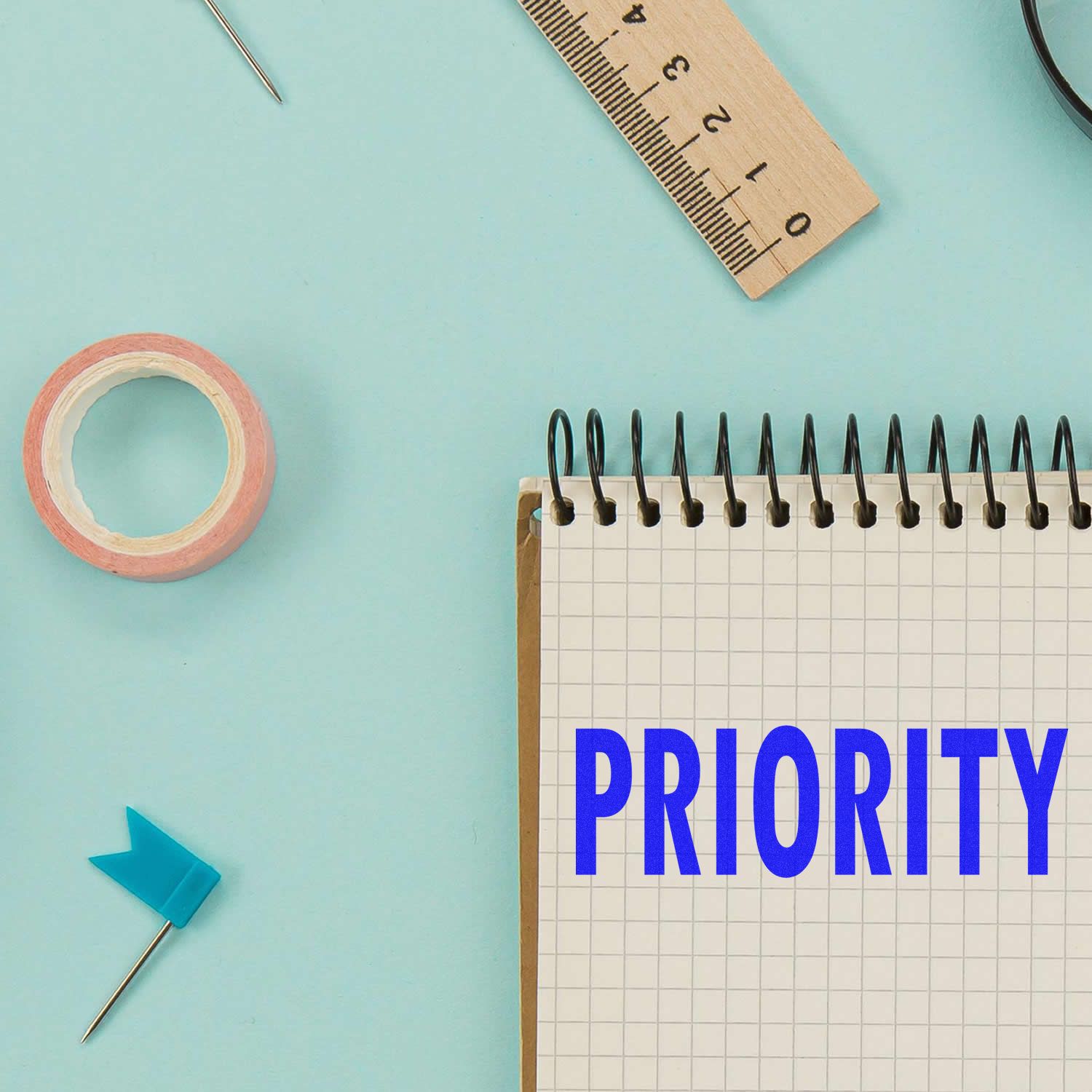 Priority written on spiral notebook with ruler, tape, and push pins on a pastel blue background, symbolizing planning and organization.