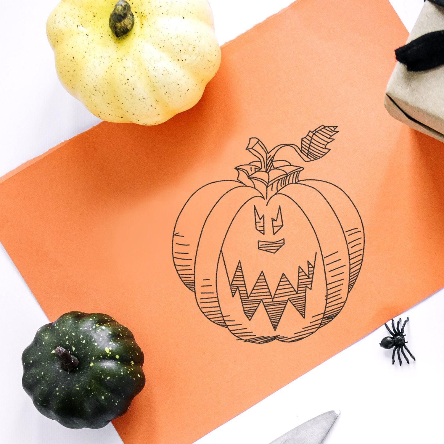 Halloween pumpkin drawing on orange paper with decorative gourds and spider craft flat lay