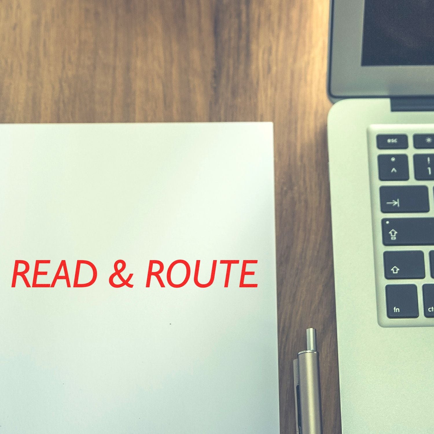 Read & Route notebook beside a laptop keyboard on a wooden desk, office workspace flat lay.