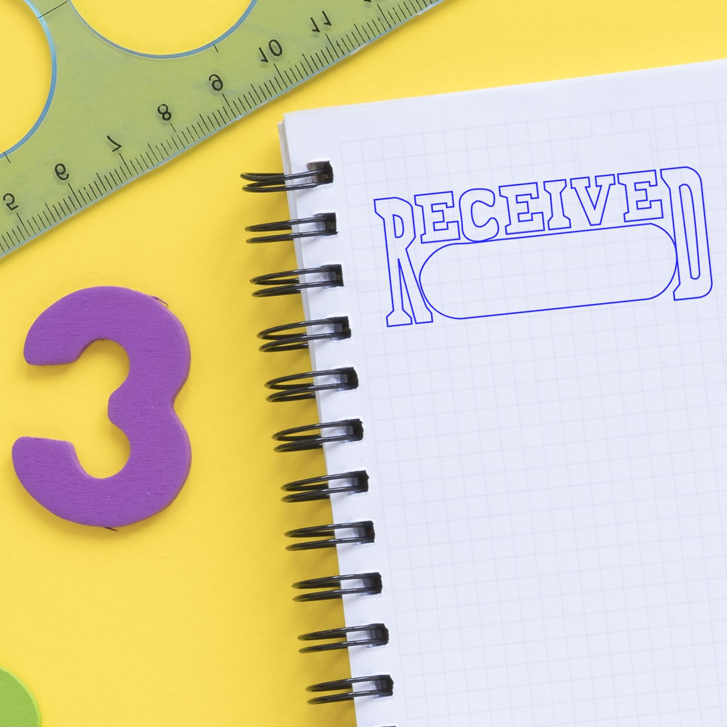 Close-up of a spiral notebook with RECEIVED text, a ruler, and colorful school supplies on a yellow background.