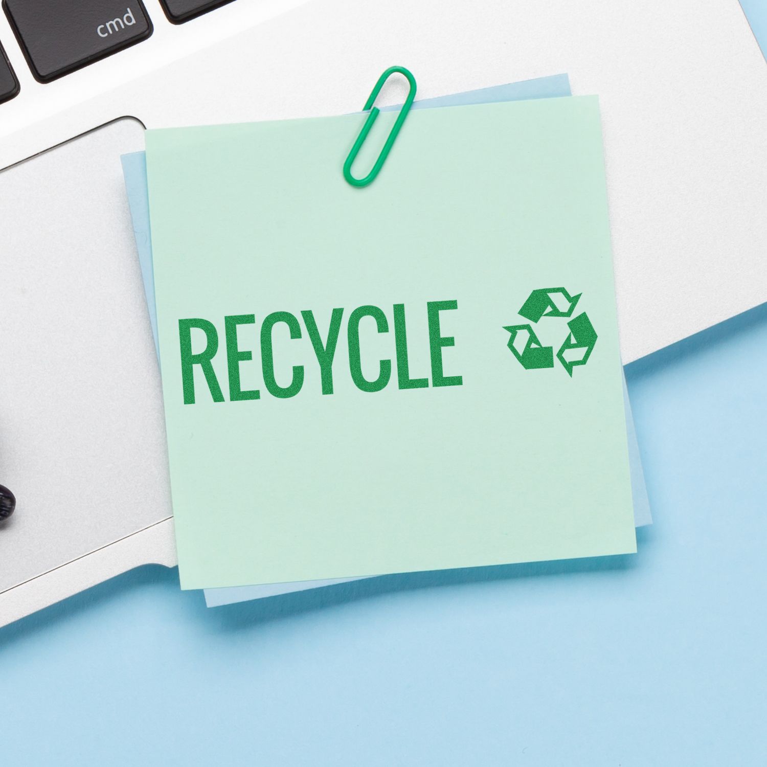 Recycling reminder note on desk with green paperclip and recycling icon, promoting eco-friendly waste management.