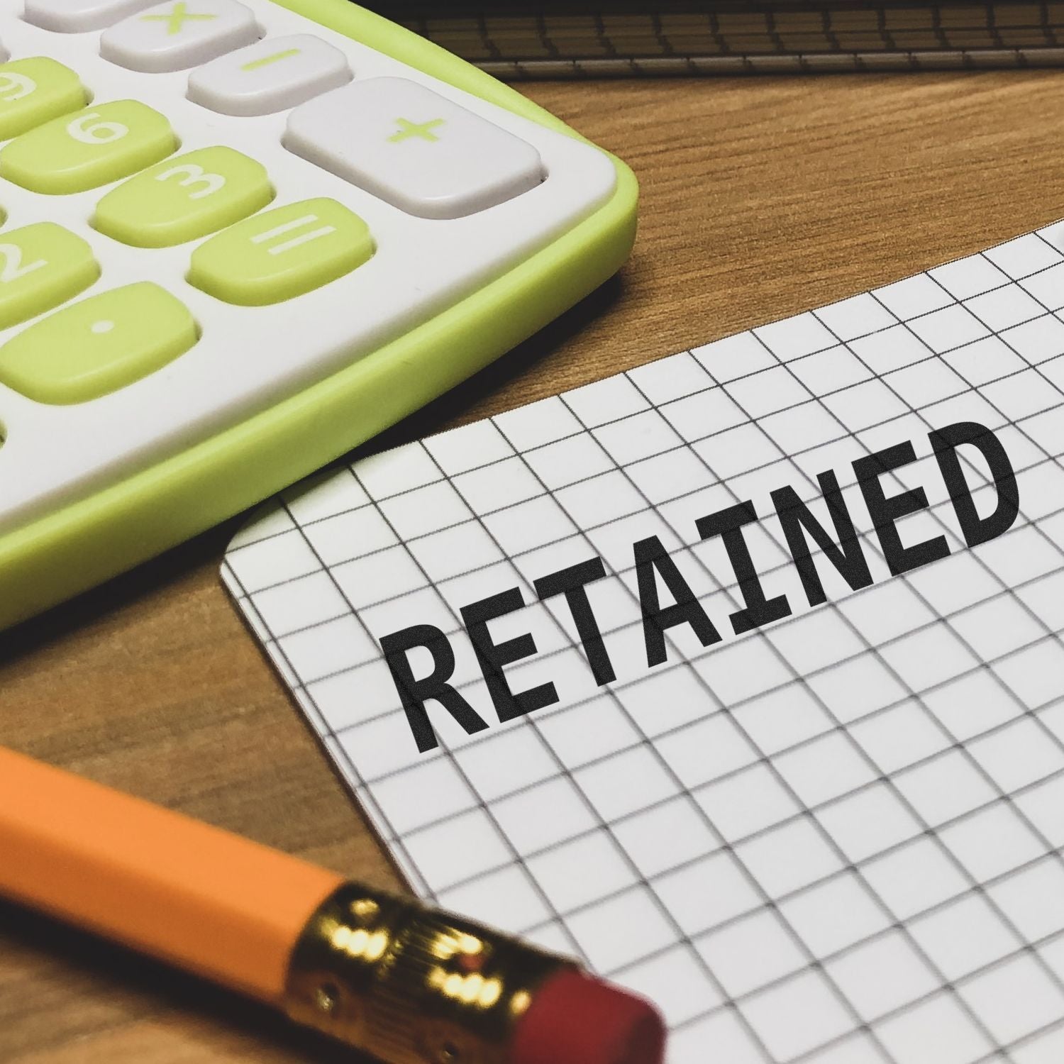 Calculator, pencil, and graph paper with RETAINED text, representing retained earnings and accounting finance concept.