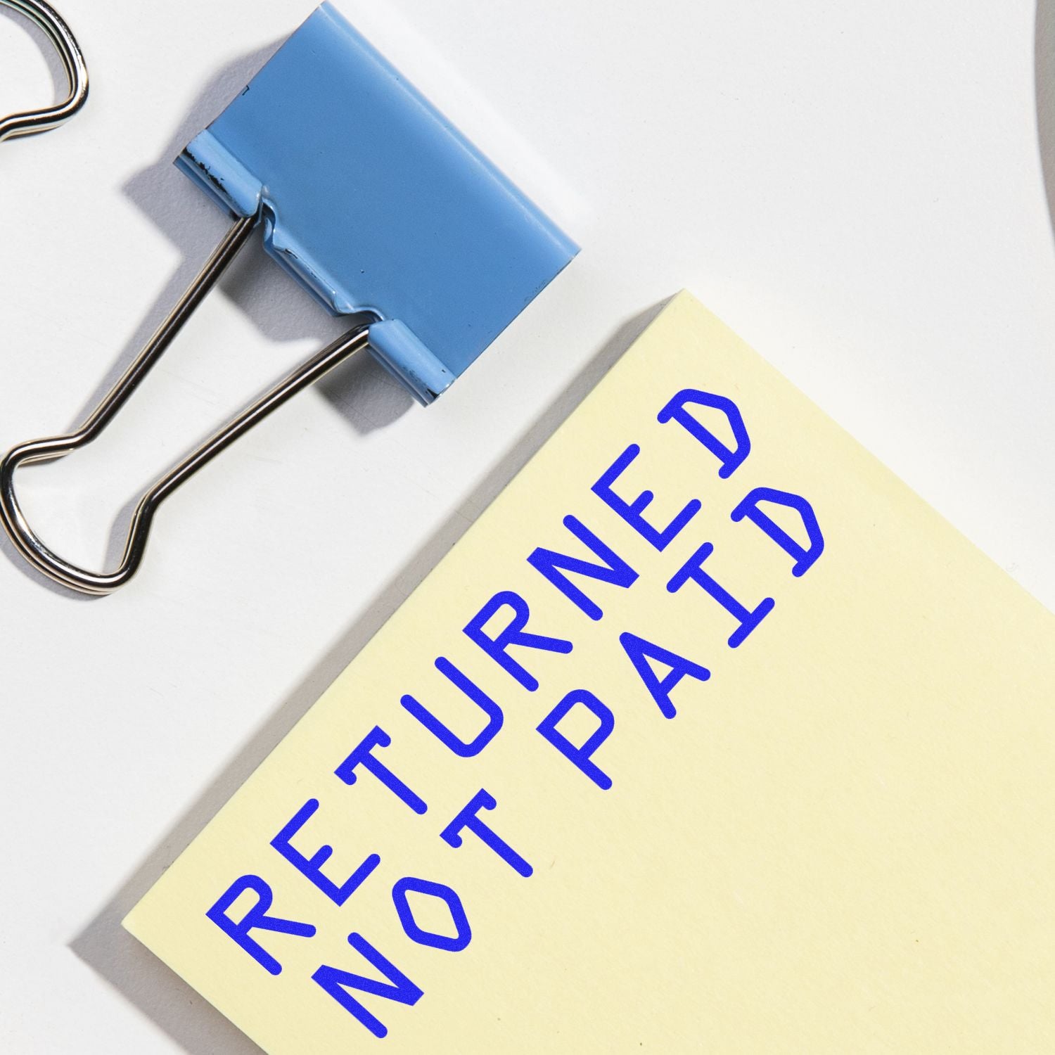 Close-up of a Returned Not Paid note clipped with binder clips, symbolizing unpaid invoice or payment rejection reminder.