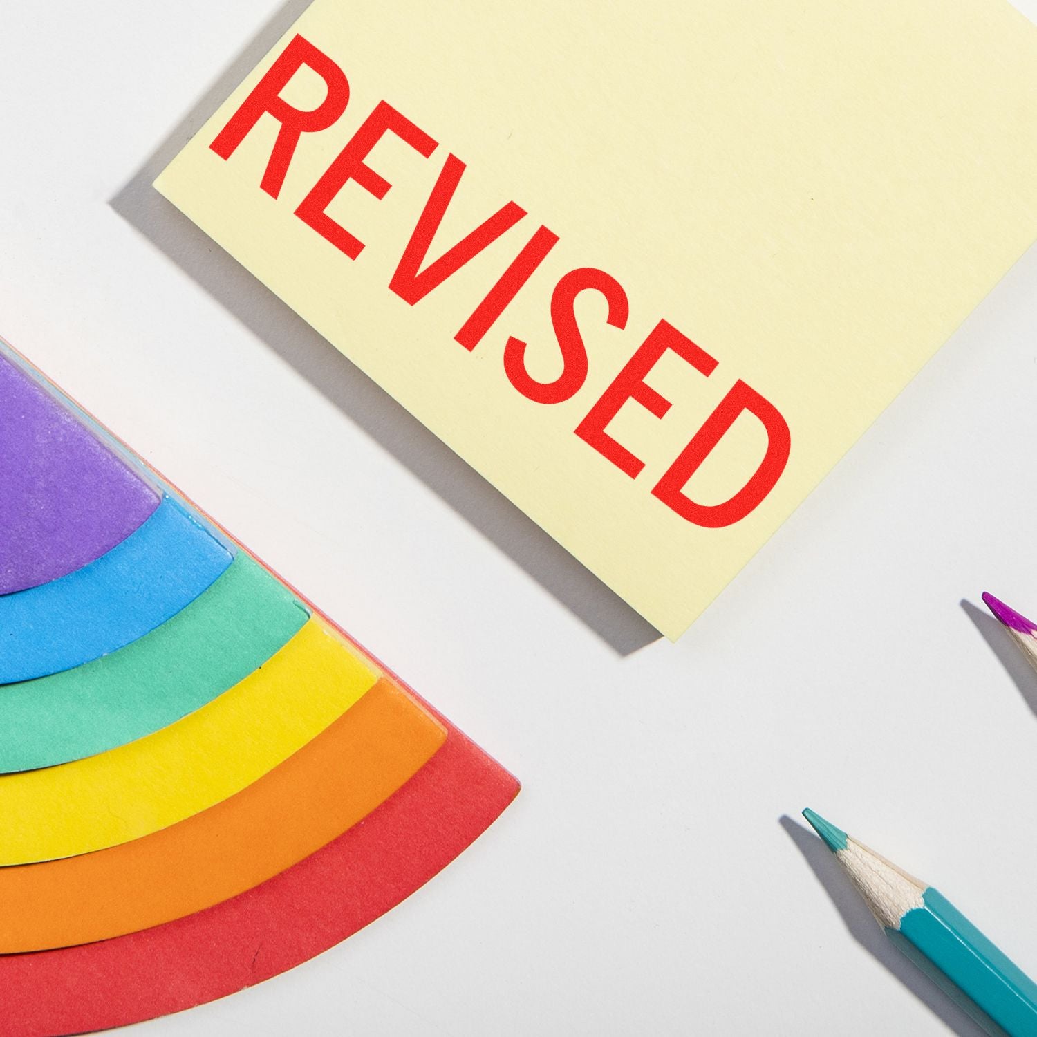 Revised note with colorful pencils and rainbow paper on a white desk background