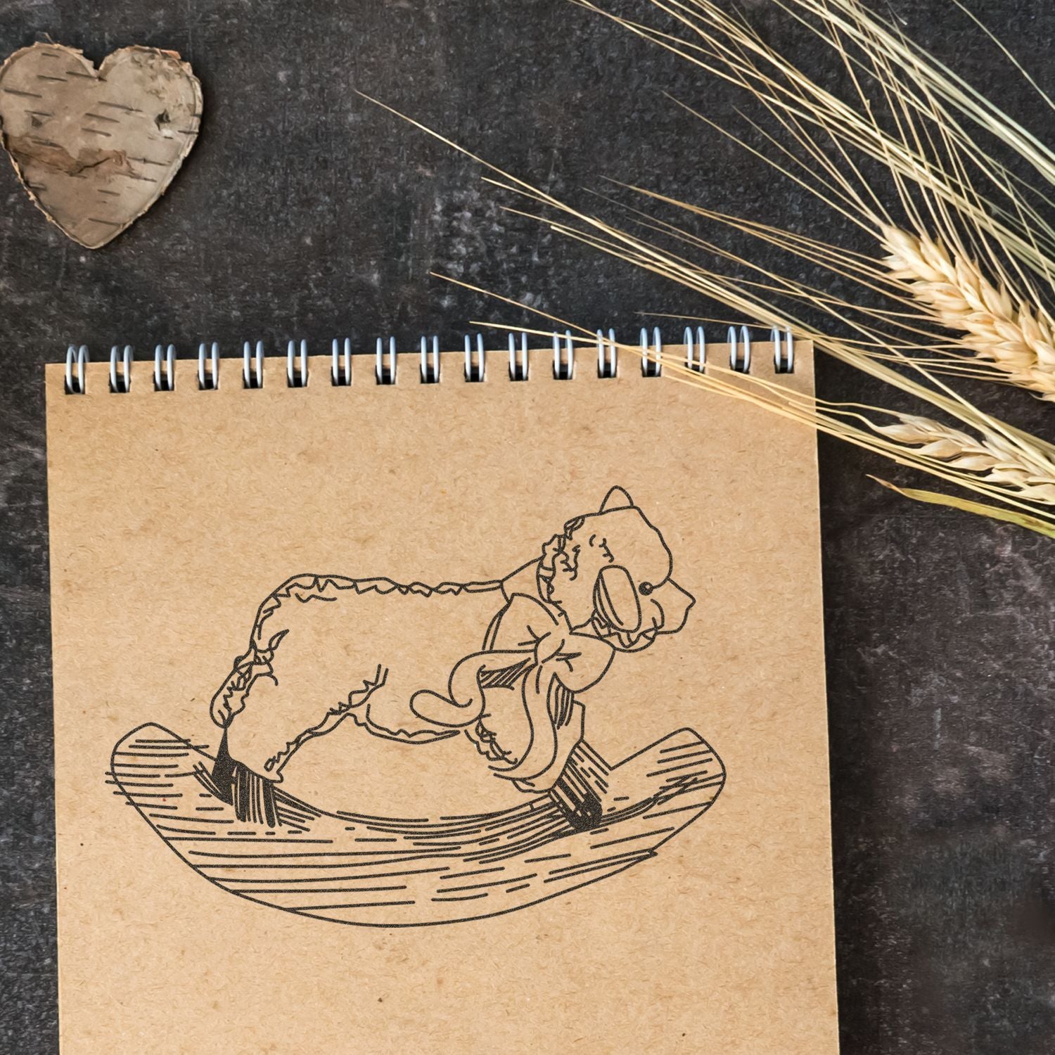 Kraft spiral notebook with cute bear on crescent moon illustration, rustic flat lay with wheat stalks and heart decor.