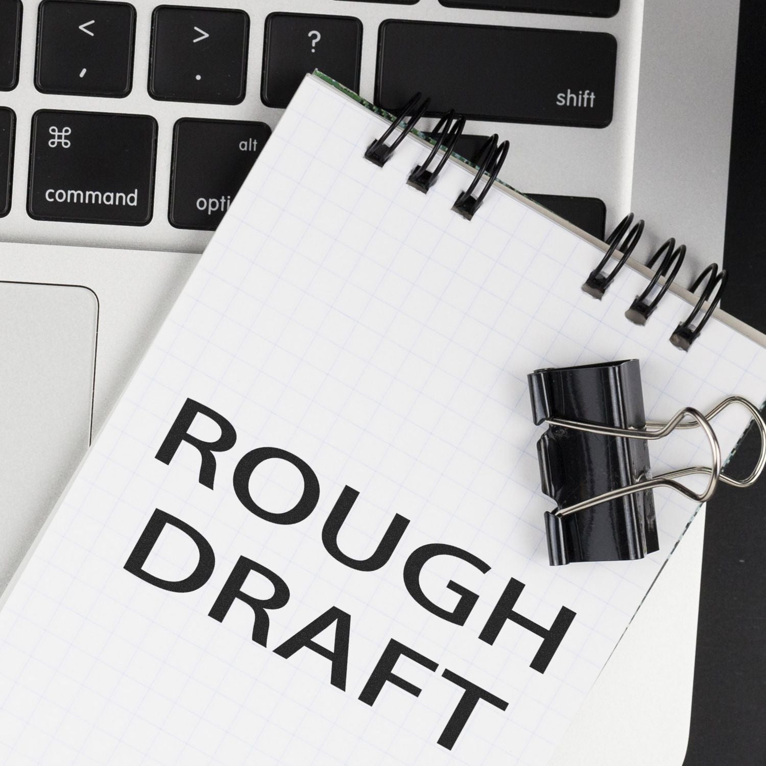 Notebook labeled Rough Draft clipped on a laptop keyboard, creative writing and editing concept.