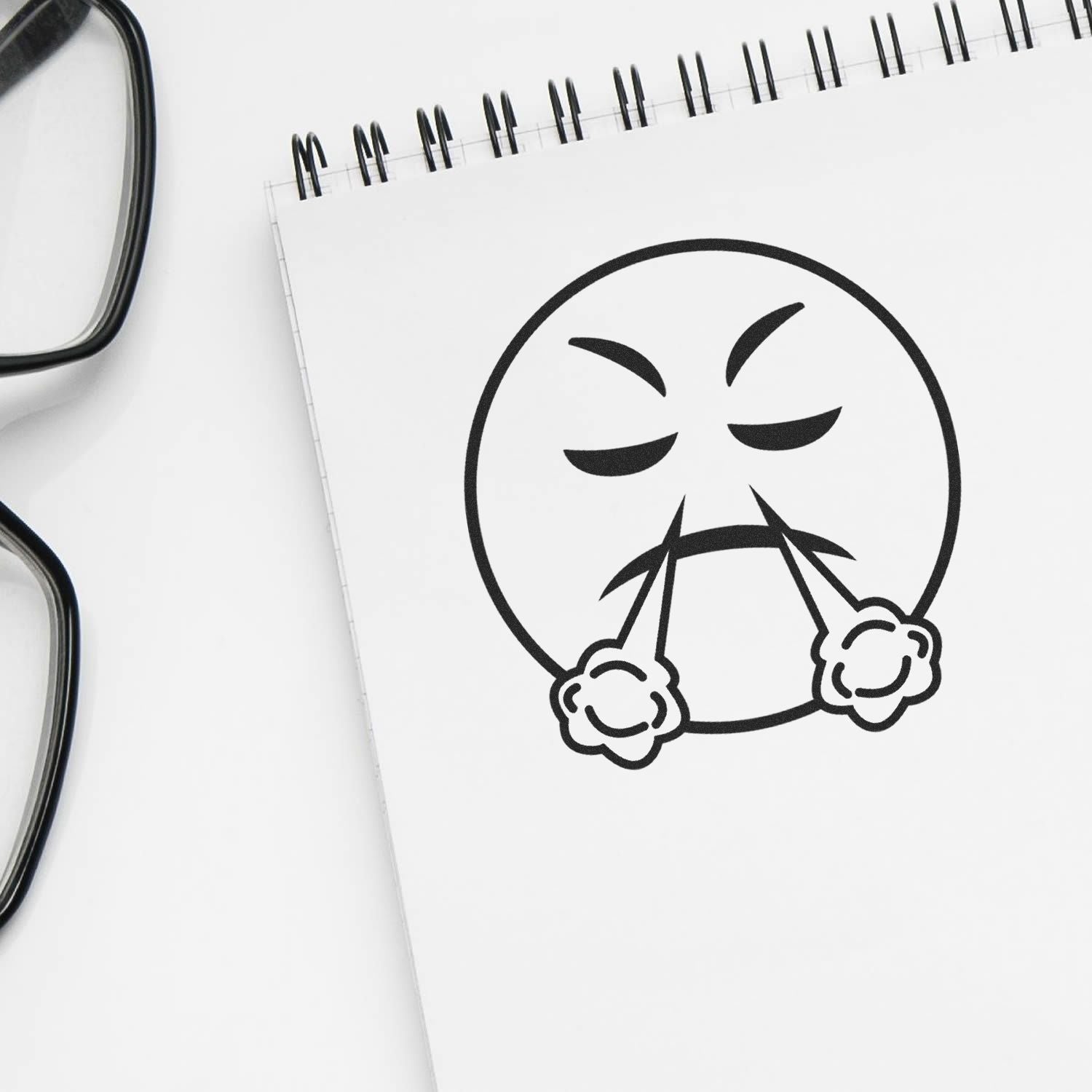 Angry emoji face drawn on a spiral notebook with eyeglasses on a white background