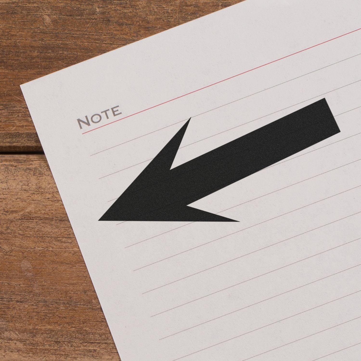 Close-up of a lined note paper with a bold black arrow on a wooden desk, minimal office stationery background.