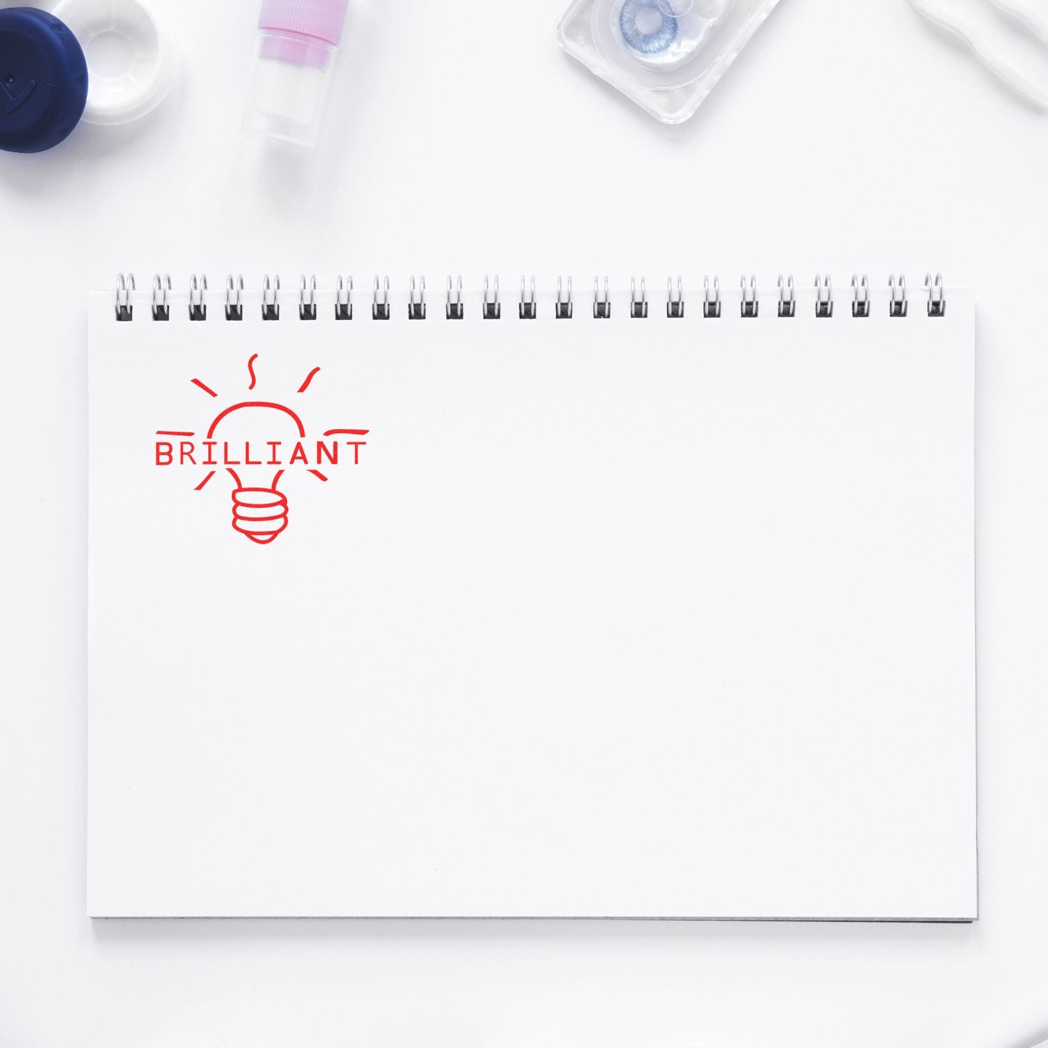 White spiral notebook with red brilliant light bulb icon on a clean minimalist desk flat lay.