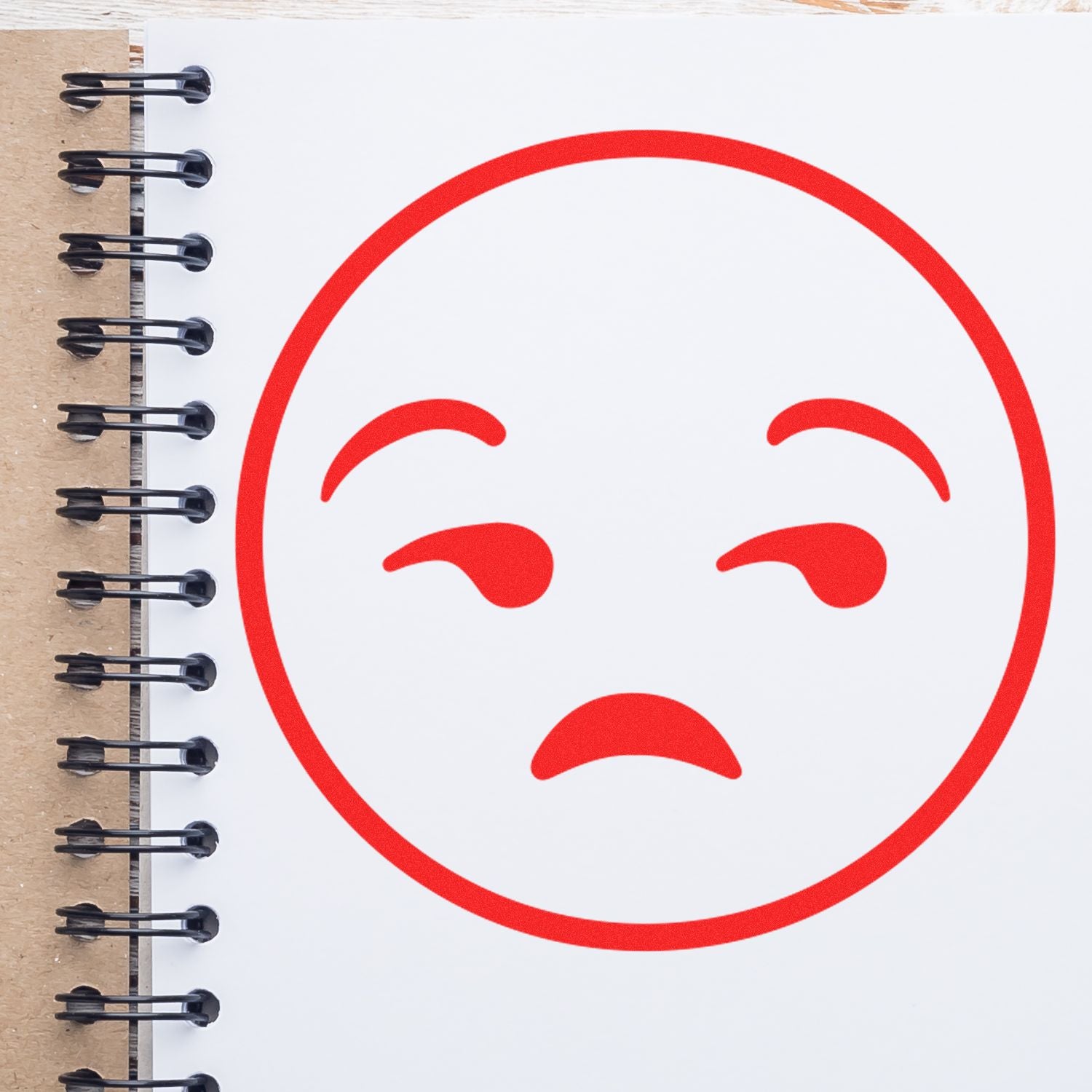 Red sad face emoji drawn on a spiral notebook page, representing disappointment or negative feedback.