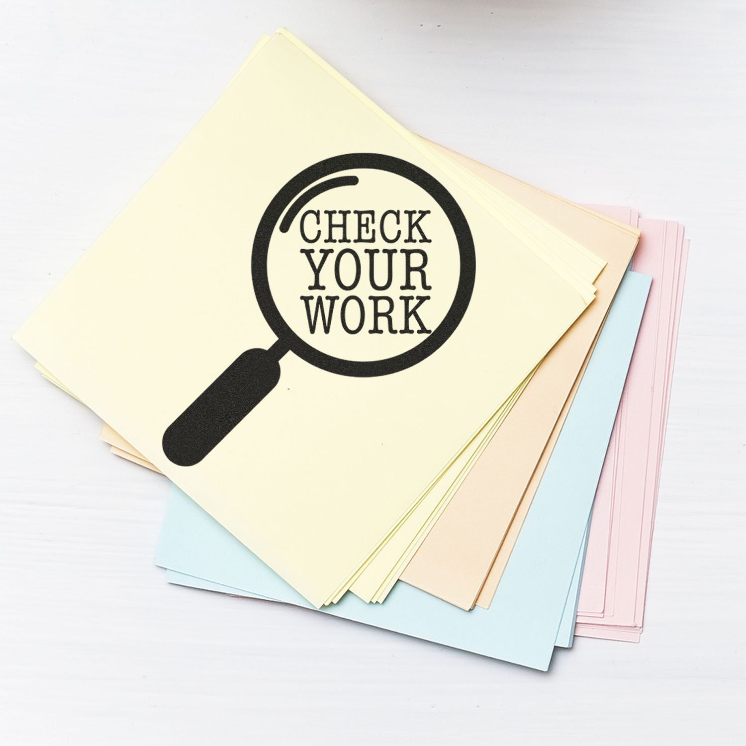 Pastel paper stack with magnifying glass icon and Check Your Work text, proofreading and editing concept.