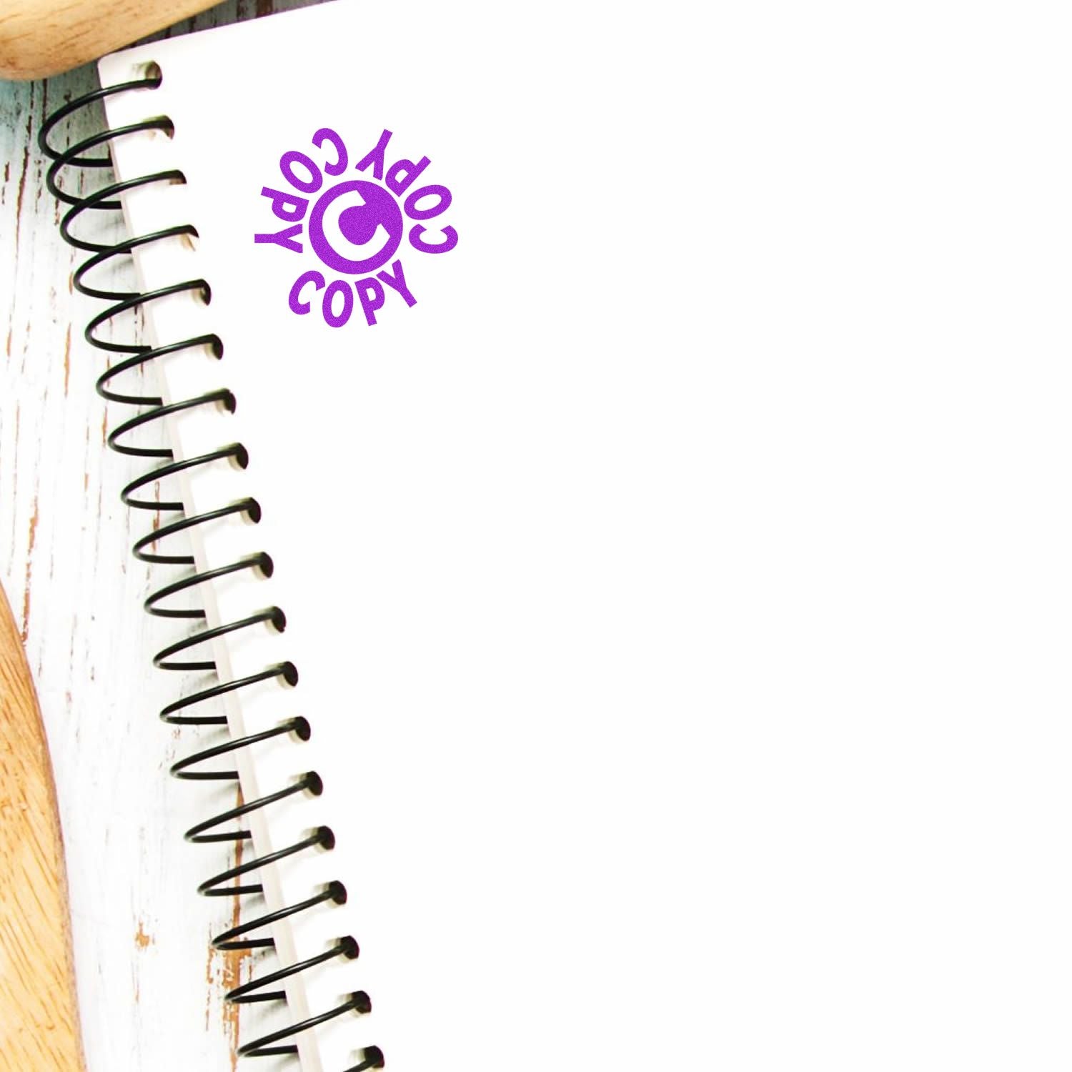 Spiral notebook with blank white page and purple copyright symbol logo on a wooden background.