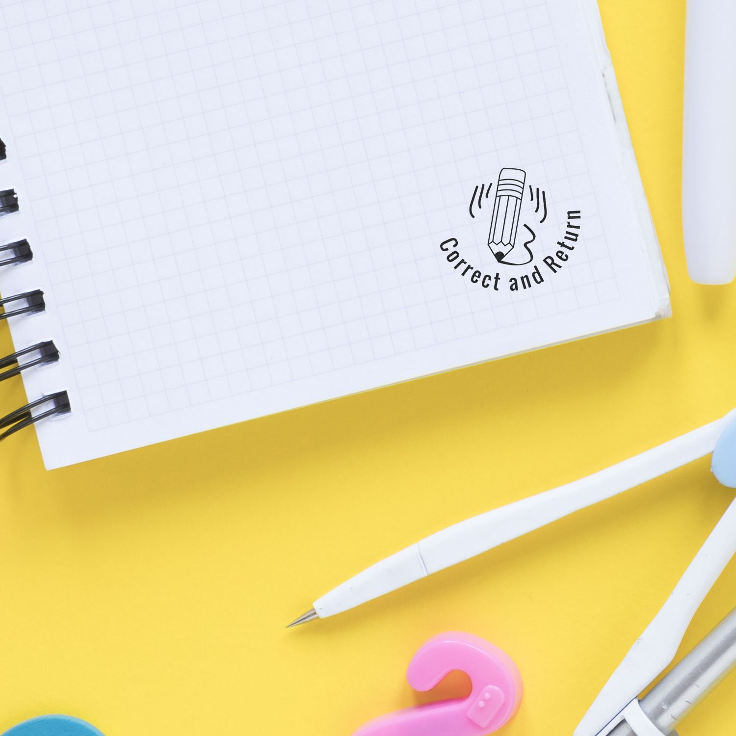 Notebook with Correct and Return stamp, pencils, and colorful stationery on a yellow background for education and office use.