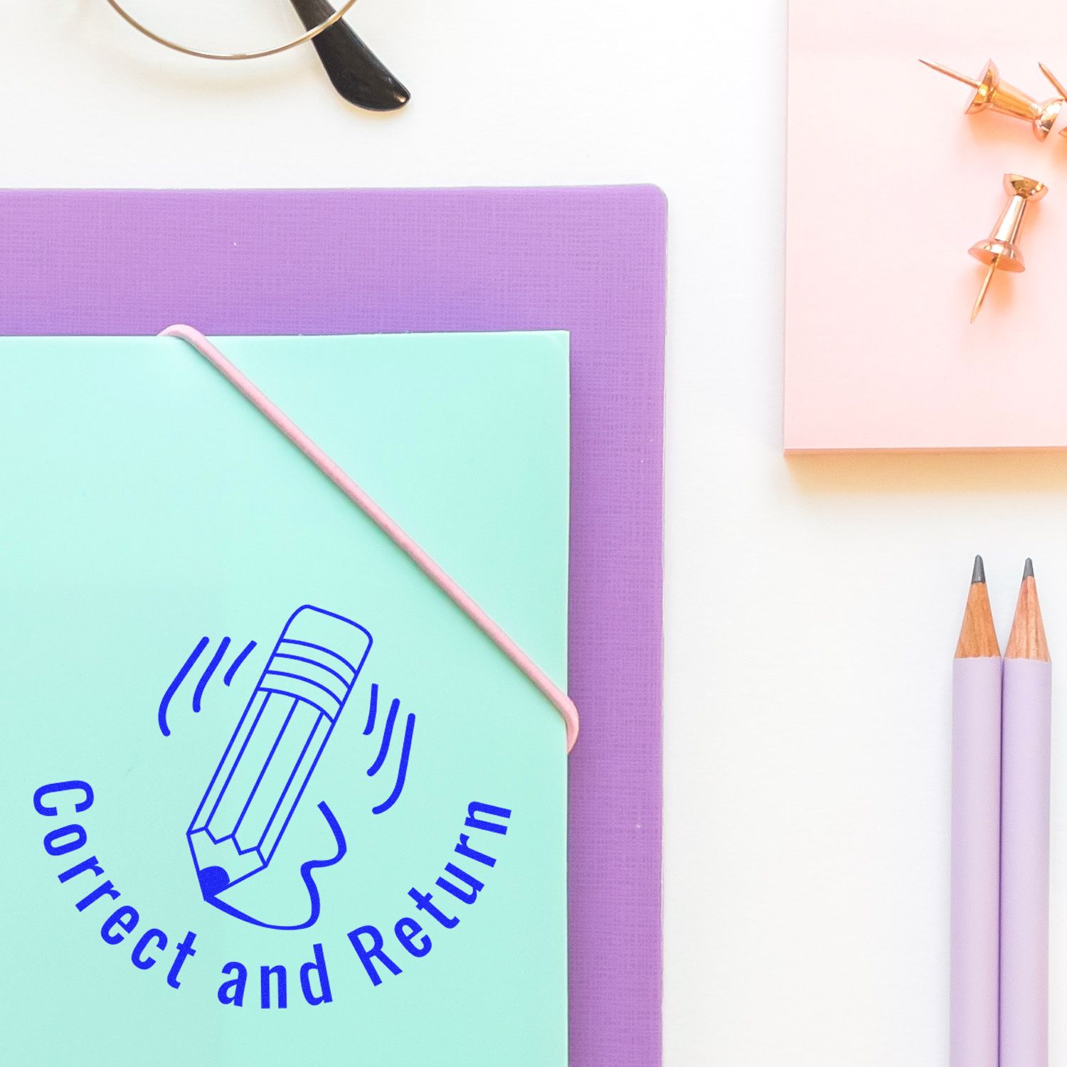 Pastel stationery flat lay with a mint Correct and Return notebook, purple folder, pencils, and gold push pins on a white desk.