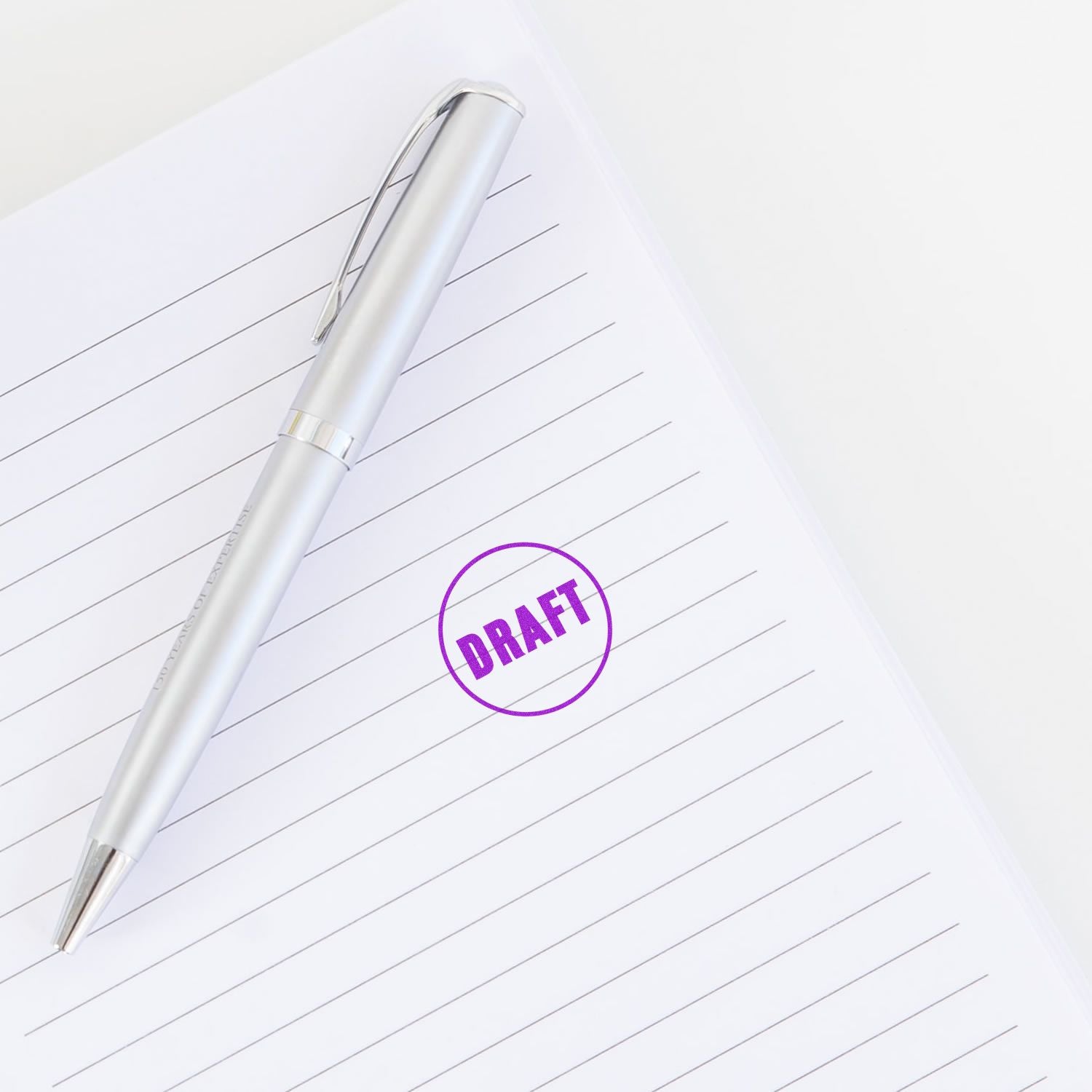 Silver pen on lined paper with purple draft stamp, concept of document editing and note taking.