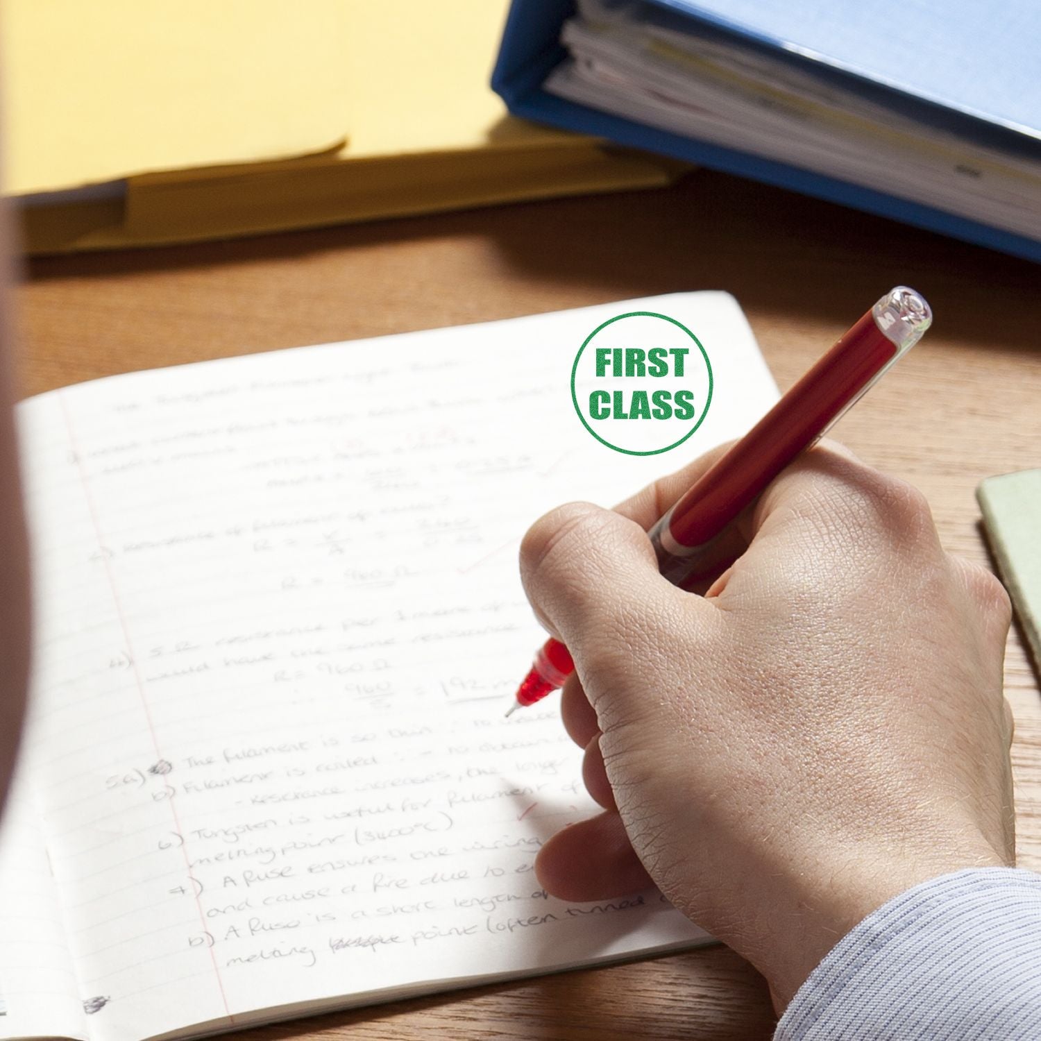 Hand writing in a notebook with a first class stamp, symbolizing academic success and high grades.