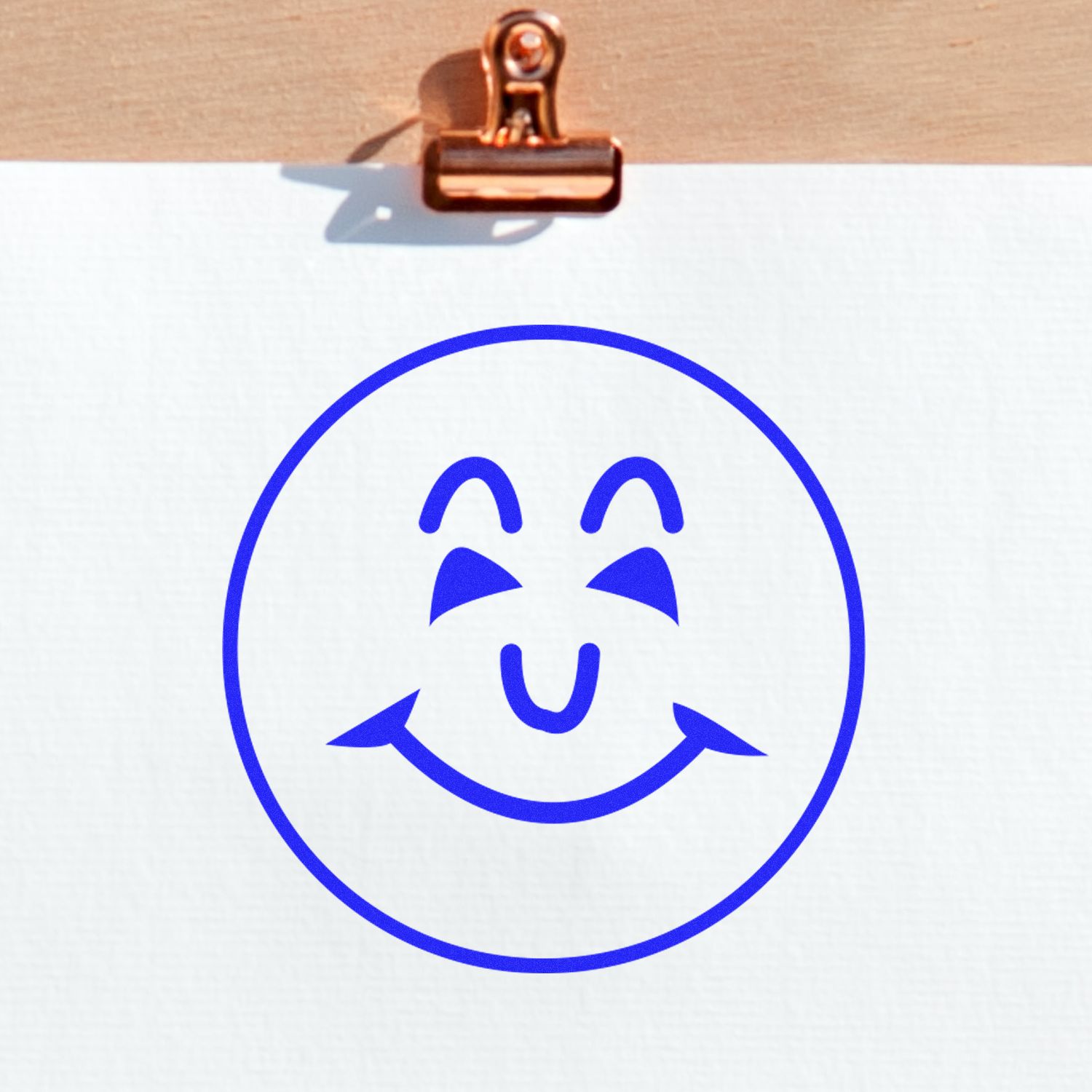 Blue smiley face drawing on white paper clipped to a clipboard, simple cheerful icon design