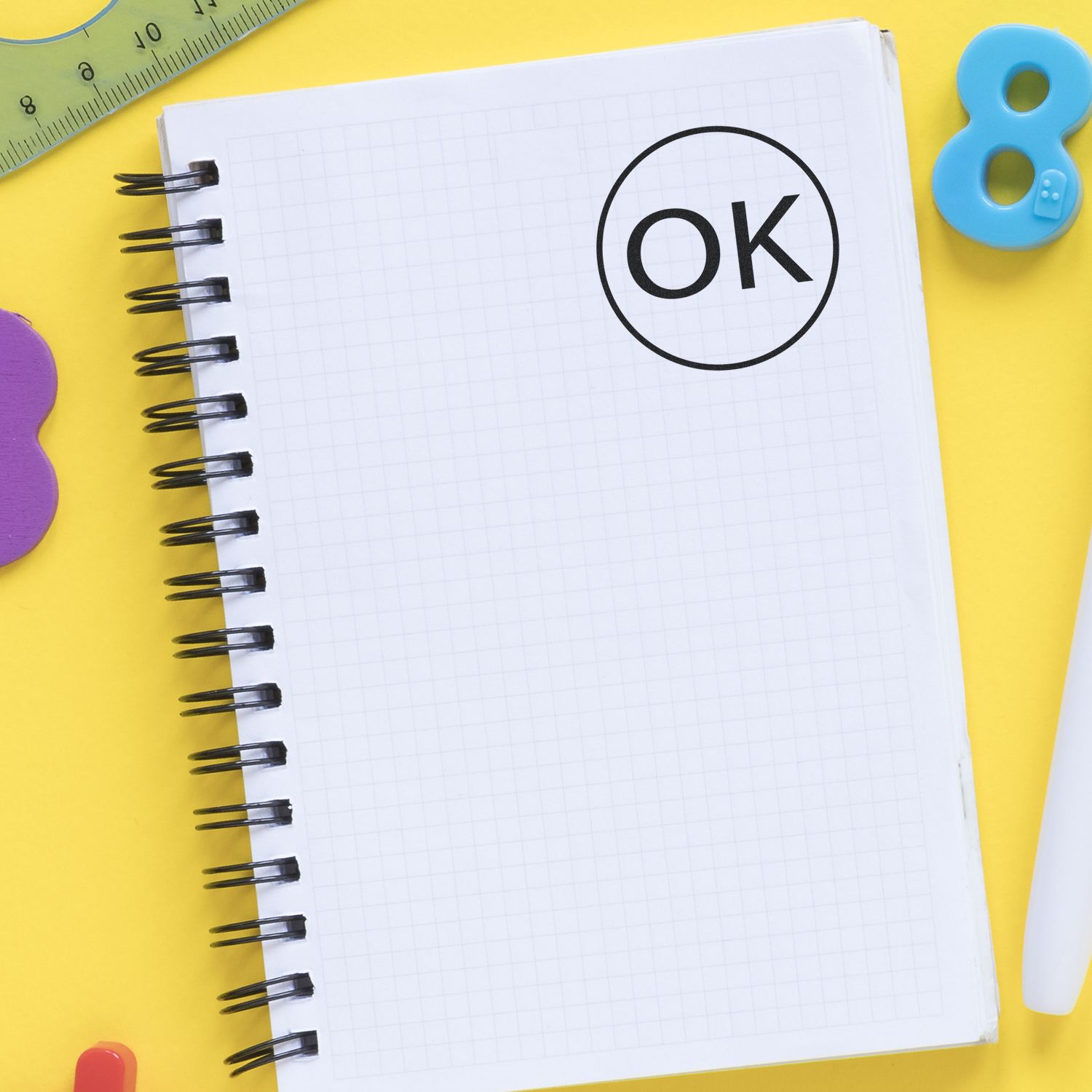 Open spiral notebook with OK symbol on yellow background, surrounded by school stationery and ruler.