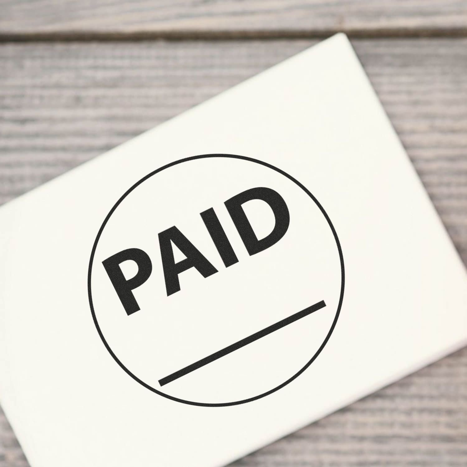 PAID stamp on paper envelope, business payment confirmation icon on wooden background.
