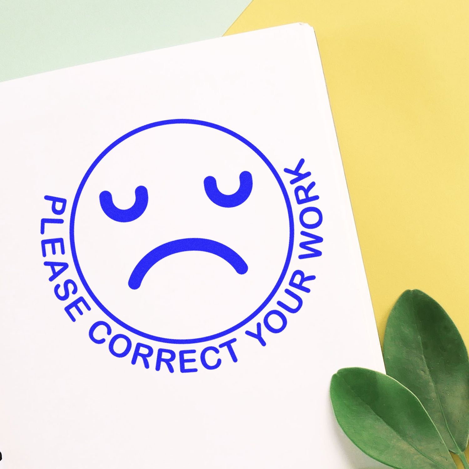 Sad face Please correct your work sign on white paper with yellow background and green leaves.