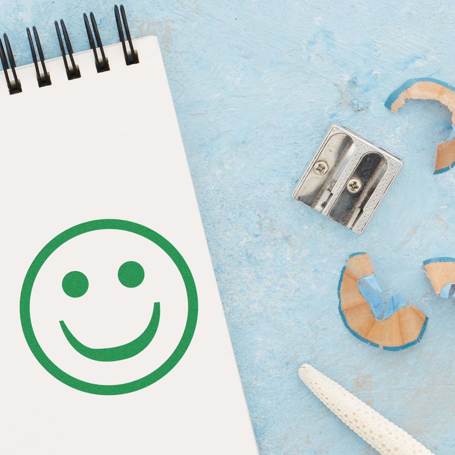 Smiley face notebook with pencil sharpener and pencil shavings on a blue textured background