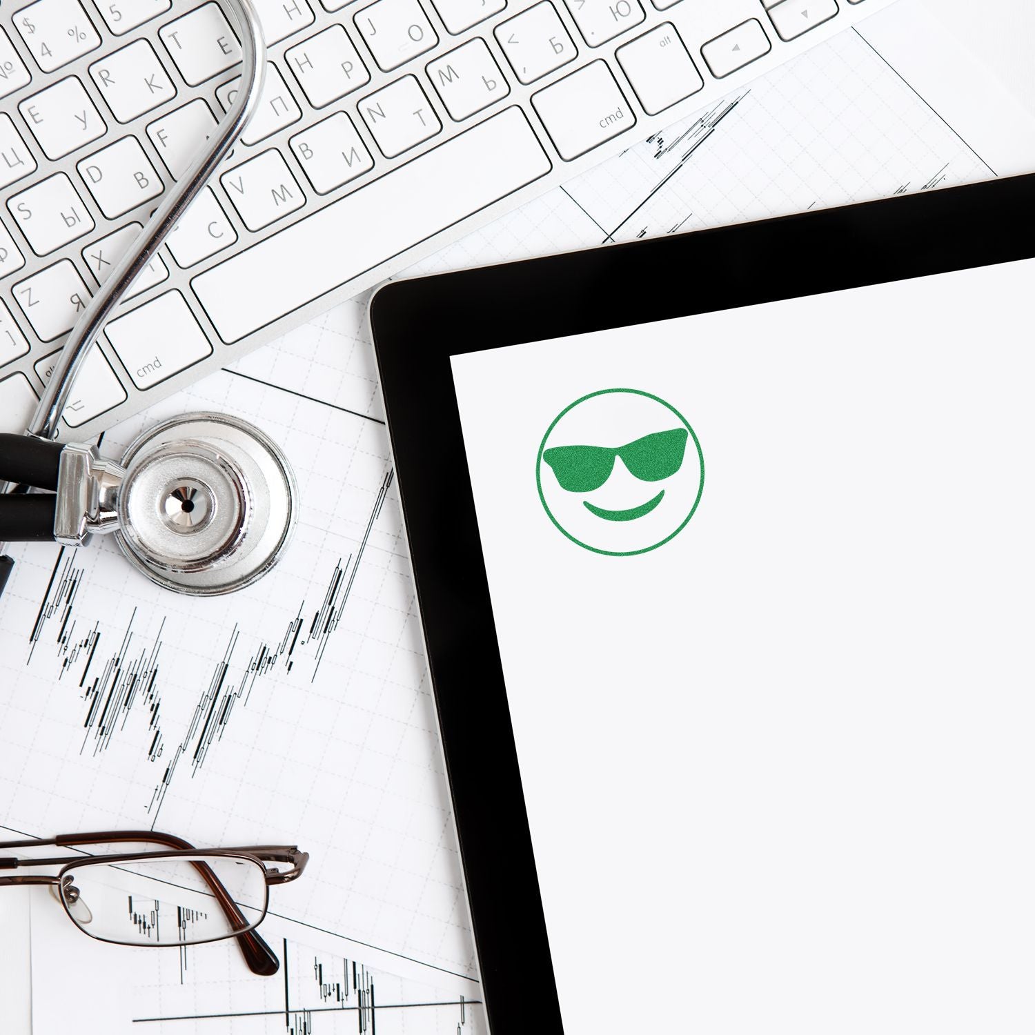 Stethoscope, keyboard, eyeglasses, and tablet with a green smiley icon over business charts, representing digital healthcare technology.