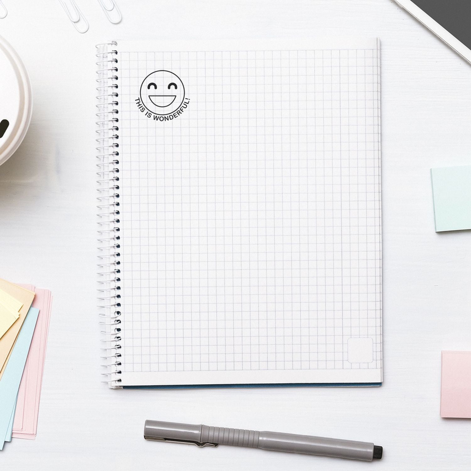Minimalist spiral notebook on a white desk with pen and pastel sticky notes, top view of a clean stationery workspace.