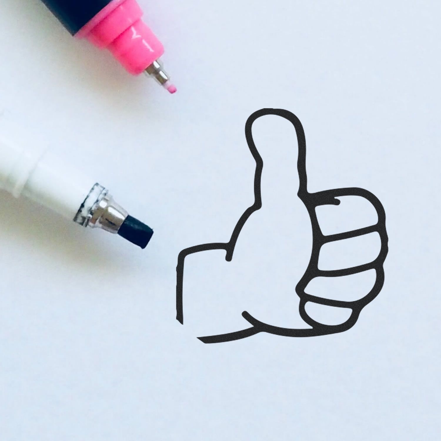 Close-up of pink and blue marker pens drawing a thumbs-up icon on a white background, creative approval concept.