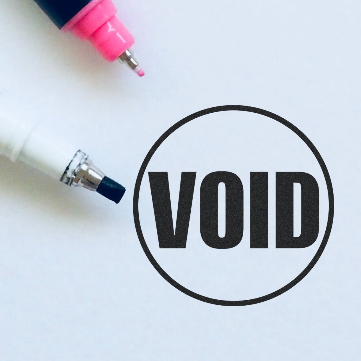 Pink and black pen tips above a bold VOID stamp on a white background, symbolizing invalid or canceled document seal.