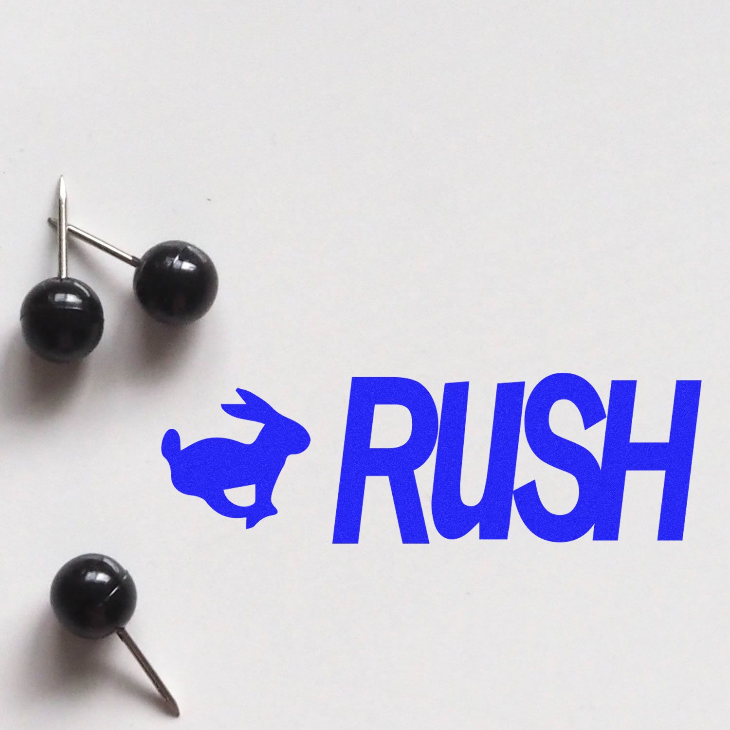 RUSH office supply branding with black push pins on white background, featuring pushpin heads and metal tips.
