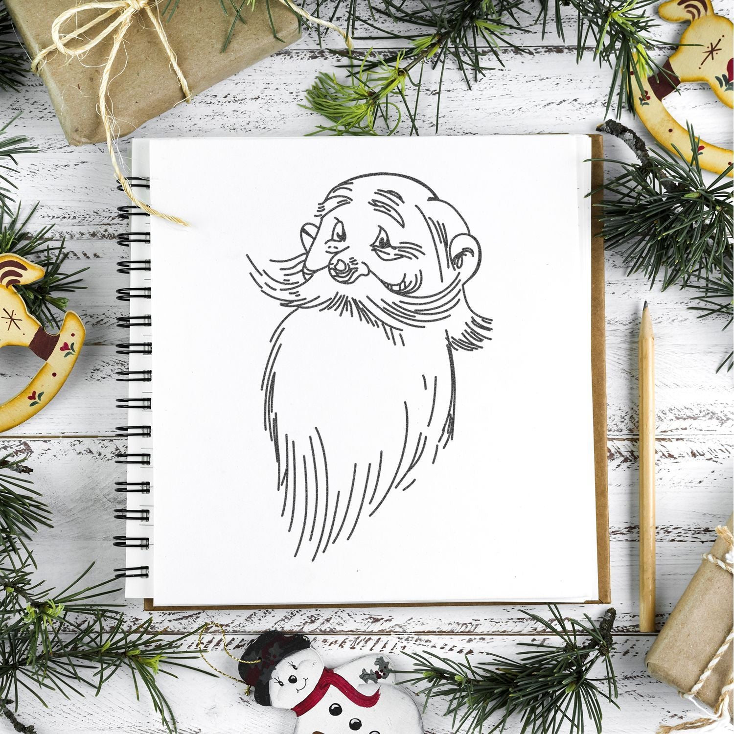 Sketchbook with Santa Claus line drawing, surrounded by Christmas greenery, ornaments, and wrapped gifts on a rustic table