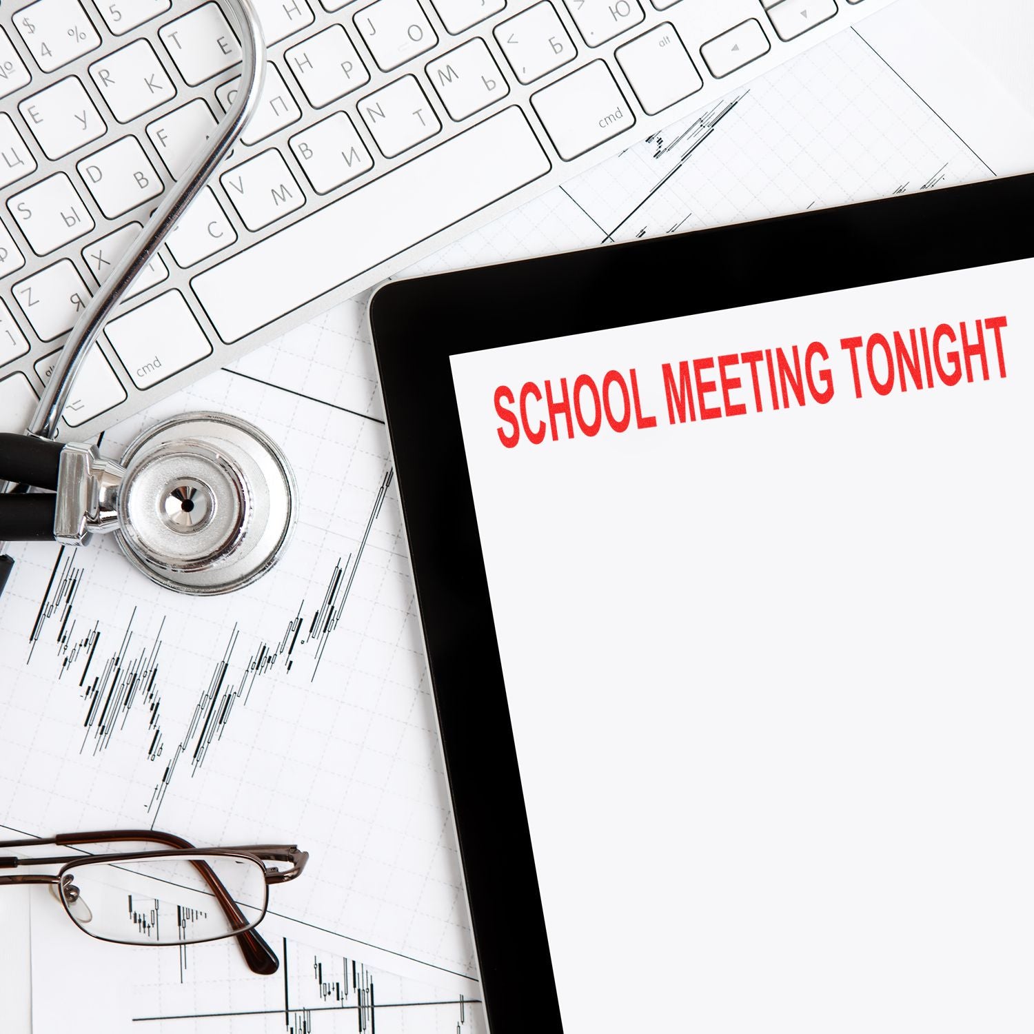 Tablet displaying School Meeting Tonight with stethoscope, keyboard, glasses, and financial charts on desk