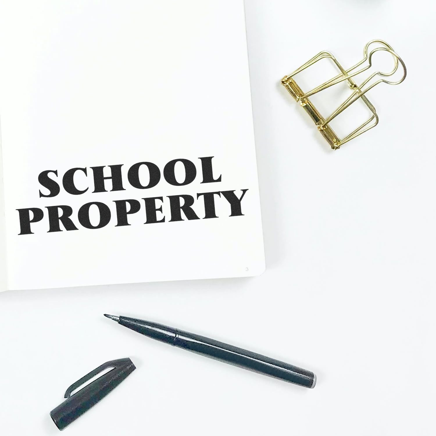 White notebook labeled SCHOOL PROPERTY with paperclip and pen, highlighting school property and classroom organization.